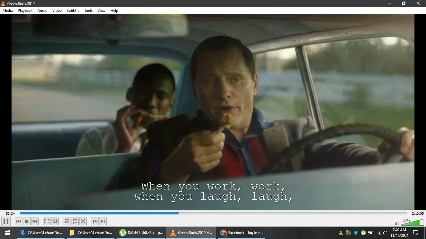 The image is a screenshot from a video playing in VLC media player, specifically from the movie "Green Book." The scene shows two men inside a car, with one man driving. The driver, Viggo Mortensen, is in the foreground, holding a piece of food while speaking to the person behind him. The passenger in the backseat is eating as well. The mood is casual and conversational, with daylight streaming through the car windows, suggesting a daytime setting. The characters appear relaxed, engaging in light-hearted conversation as they travel. The seat and interior of the car are visible, with simple, muted colors contributing to the scene's realistic feel. The subtitle at the bottom reads, "When you work, work, when you laugh, laugh," capturing part of the dialogue and adding to the scene's context. The overall composition highlights a moment of camaraderie and humor between the characters.
- Site / app: "VLC media player"
- Captions / subtitles: "When you work, work, when you laugh, laugh,"