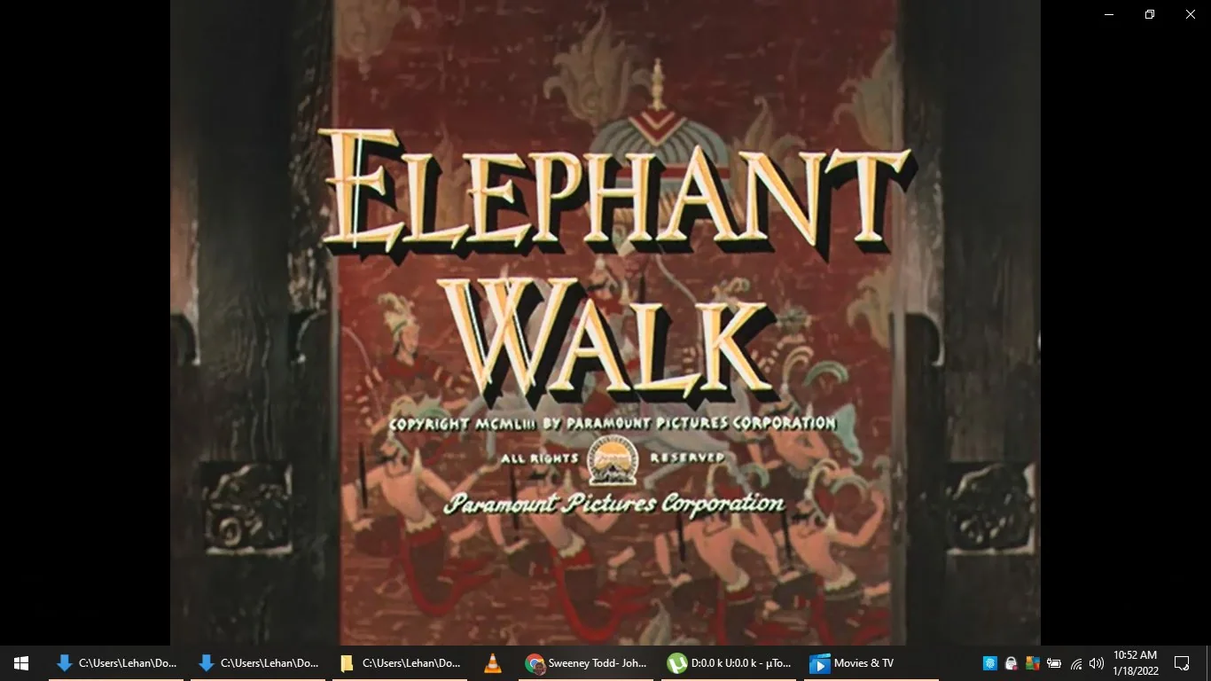 This image is a title screen from the movie "Elephant Walk," released by Paramount Pictures Corporation. The text "ELEPHANT WALK" is prominently displayed in large, stylized lettering, set against a decorative background featuring traditional artistic motifs that appear to be inspired by Asian or tropical themes, possibly hinting at the movie's setting. Beneath the title, the copyright notice is visible, stating "Copyright MCMLIII by Paramount Pictures Corporation," which indicates the movie was released in 1953. The background features intricate designs, potentially depicting cultural or historical scenes, which add to the exotic ambiance of the movie's theme. The colors are rich and warm, predominantly reds and browns, creating a sense of depth and intrigue. This title screen effectively sets the tone for a classic film experience, offering a glimpse into the style and presentation typical of mid-20th-century cinema. The framing and composition focus solely on the text and background artwork, making it clear and impactful for the audience.