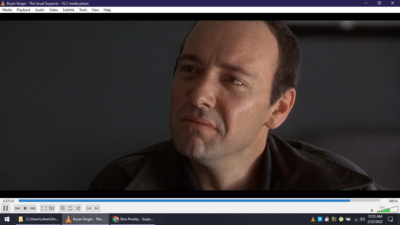 The image is a screenshot from the film "The Usual Suspects," directed by Bryan Singer, as displayed on the VLC media player. The scene features a close-up of Kevin Spacey, portraying a character from the film. He appears to be in an indoor setting, with a neutral, slightly contemplative expression on his face. The lighting is soft, casting gentle shadows that highlight his features.
The VLC media player interface is visible, showing the playback bar at the bottom, with controls like play, pause, and volume. The time stamp indicates that the scene is near the end of the movie. The Windows taskbar at the bottom of the image shows the current time and date as 12:55 AM on February 22, 2022. The title at the top of the window reads "Bryan Singer - The Usual Suspects - VLC media player."
This particular frame captures a moment of introspection or revelation, characteristic of the film's intricate plot and character development.