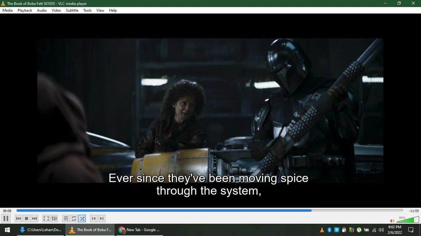 1) The screenshot captures a scene from the episode titled "The Book of Boba Fett S01E05," viewed using VLC media player. In an indoor setting, the image shows two characters engaged in conversation. On the left, a person with curly hair sits slightly forward, gesturing with their hands, suggesting engagement or explanation. On the right, a character in black Mandalorian armor holds a weapon. This armor is iconic within the Star Wars universe, reflecting the character's affiliation and role. The lighting is dim, creating a dramatic, sci-fi atmosphere typical of the series. The background reveals a workshop-like environment with machinery, reinforcing the setting's industrial feel. Subtitles at the bottom read, "Ever since they've been moving spice through the system," indicating dialogue related to storyline themes of trade or smuggling. The display features typical VLC interface elements, like the title at the top and playback controls at the bottom, confirming the media player being used.
2) On-screen text block:
- Title: "The Book of Boba Fett S01E05 - VLC media player"
- Captions / subtitles: "Ever since they've been moving spice through the system,"