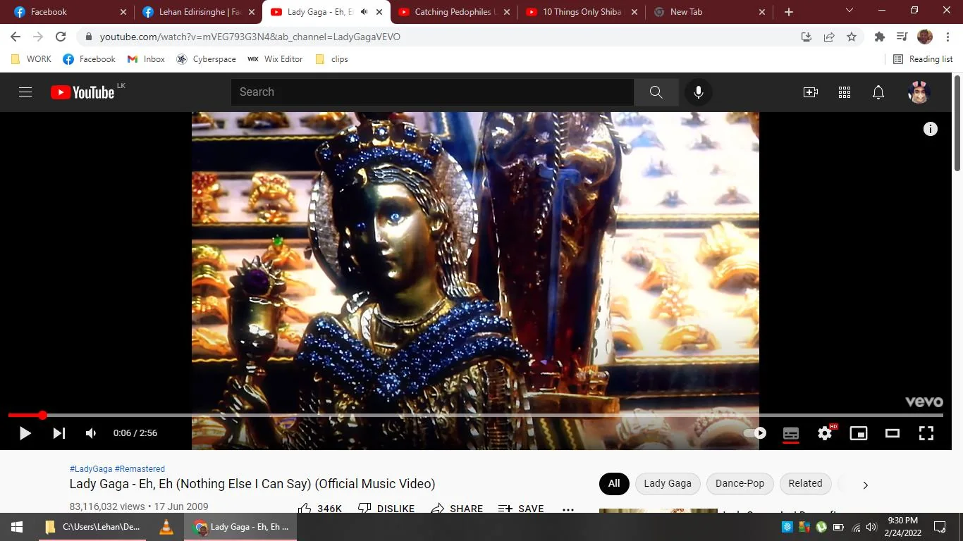 The image is a screenshot from the YouTube video player displaying the official music video for "Eh, Eh (Nothing Else I Can Say)" by Lady Gaga. The timestamp is at 0:06 out of a total 2:56 duration. The video, published on the LadyGagaVEVO channel, has accumulated over 83 million views as of the screenshot date. The visual depicts an ornate statue adorned with intricate details, including gold and blue embellishments, a crown, and what appears to be a decorative background filled with jewelry or similar ornate items. The bright lighting highlights the reflective surfaces, emphasizing the luxuriousness of the scene. The YouTube interface is visible, including the play button, video title, view count, and publication date. The video is associated with tags like "LadyGaga," "Remastered," and "Dance-Pop," indicating the genre and remastered nature of the content.