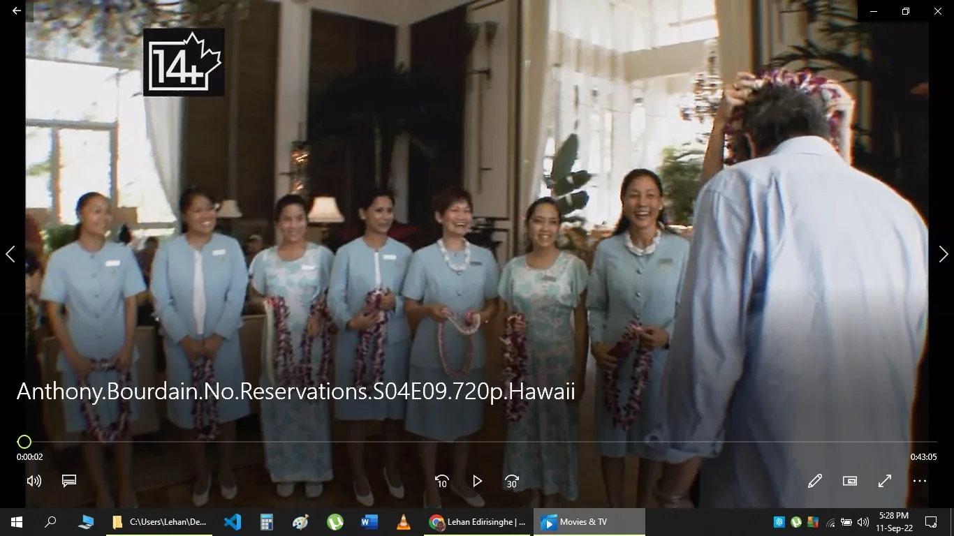 The image is a screenshot from an episode of "Anthony Bourdain: No Reservations," specifically from the Hawaii episode in Season 4. In the scene, a group of women dressed in light blue uniforms are welcoming a man, who appears from behind, by placing a lei around his neck. This traditional Hawaiian greeting is conducted indoors, likely at a hotel or resort, given the elegant decor and large windows allowing daylight to illuminate the space. The women are smiling warmly, indicating a friendly and hospitable atmosphere. The man, identified in the context as Anthony Bourdain, is wearing a casual light blue shirt. The scene captures a moment of cultural greeting, highlighting the warmth and hospitality typical of Hawaiian customs. The setting is bright and well-decorated, with plants and soft lighting contributing to the welcoming environment. The file name at the bottom of the image confirms the show's title and episode details.
- Title: "Anthony.Bourdain.No.Reservations.S04E09.720p.Hawaii"
- Site / app: "Movies & TV"