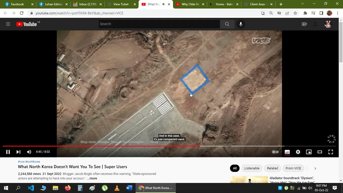 This screenshot captures a scene from a YouTube video titled "What North Korea Doesn’t Want You To See | Super Users," published by VICE. The image displays an aerial or satellite view of a terrain, possibly a part of North Korea, as suggested by the video title. The composition features a patch of land with a square marked in blue, indicating a specific area of interest. Adjacent to this marked area is a section resembling an airstrip or runway, characterized by a striped pattern typical of airport runways.
The landscape appears barren with earthy tones of brown and beige, indicating a dry or undeveloped area. Some faint structures and pathways can be seen in the surrounding terrain, suggesting minimal human activity or development. Annotations on the screen include map data credits to Google and Maxar Technologies for the year 2022. Captions at the bottom provide context, stating, "And in this case, it's just compacted sand," likely referring to the marked area. The video seems to explore themes related to geographical or political insights about North Korea, as reflected by the topic tags #vice and #northkorea.
- Title: "What North Korea Doesn’t Want You To See | Super Users"
- Channel / profile: "VICE"
- Site / app: "YouTube"
- Captions / subtitles: "And in this case, it's just compacted sand."