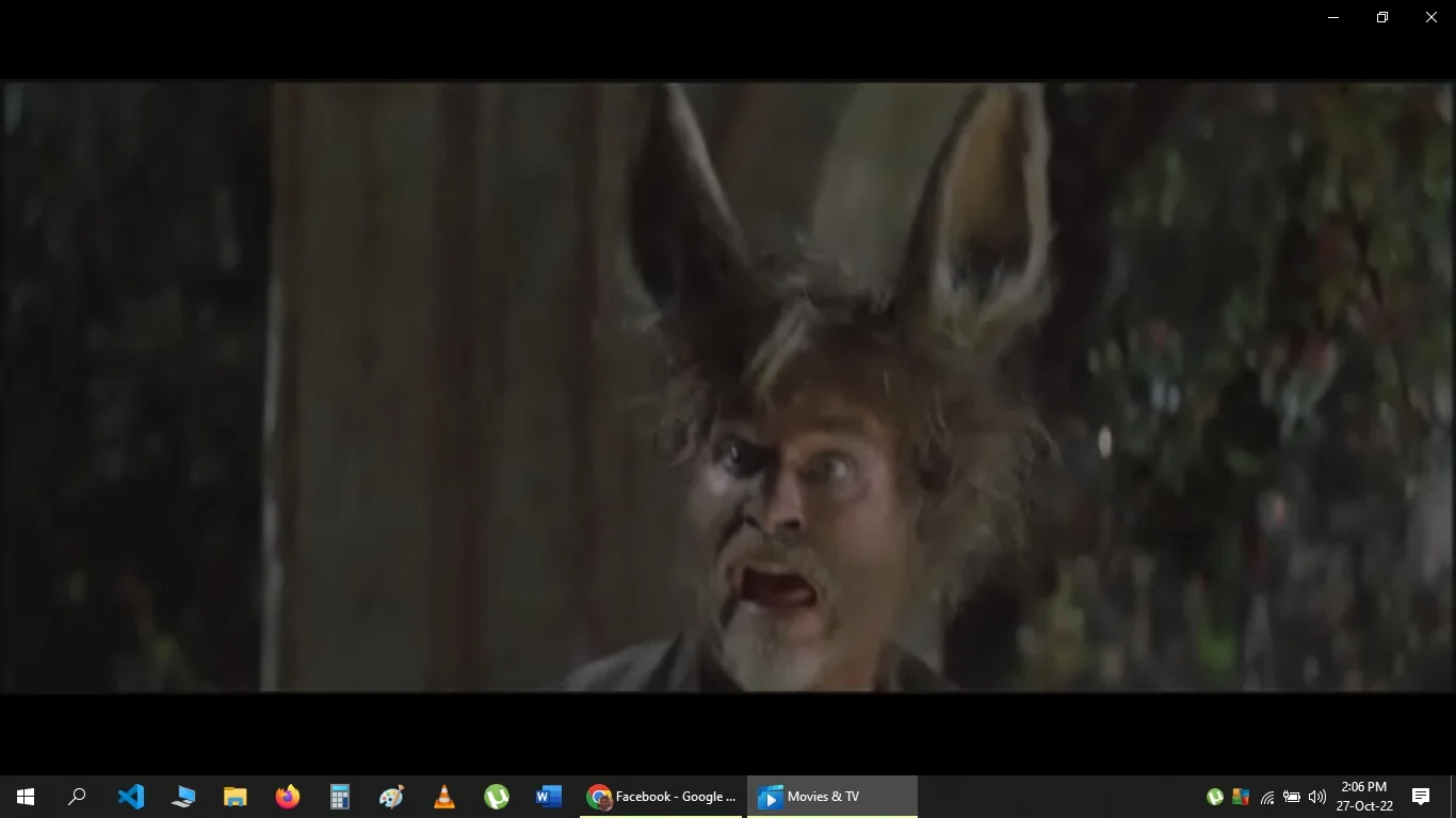 This image is a video frame from a movie or TV show, viewed on the "Movies & TV" app. It features a character with exaggerated, animal-like features, such as large ears and a hairy face, resembling a donkey or similar creature. The character appears to be outdoors, possibly in a wooded or garden setting, as indicated by the blurry foliage in the background. The lighting is somewhat dim, suggesting a nighttime scene.
The character's expression is animated and comical, with wide eyes and an open mouth, conveying surprise or confusion. The costume and makeup are designed for a fantasy or transformation theme, typical of adaptations with magical or mythical elements.
The screenshot includes a visible taskbar and other open applications, indicating a computer or laptop screen. The text at the bottom of the screen appears to be part of a truncated message from a conversation, mentioning names like "Sujeewa Nelson" and "Shavendra," but it's unrelated to the scene's content. The message itself seems to discuss political topics humorously.