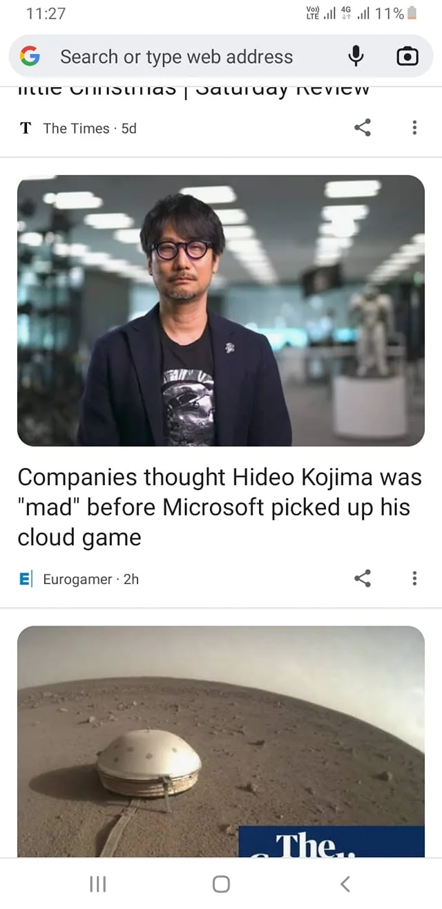---
This image features Hideo Kojima, as indicated by the hint, captured in what appears to be an indoor, modern office setting. Kojima is wearing a dark blazer over a graphic T-shirt, and glasses, giving a professional yet creative appearance. The background is softly blurred, highlighting Kojima in sharp focus, with what looks like a futuristic sculpture or model visible in the back, adding to the technological atmosphere. The lighting is bright and evenly spread, typical of an office environment.
The headline beneath the image reads, "Companies thought Hideo Kojima was 'mad' before Microsoft picked up his cloud game," suggesting a narrative about skepticism toward his innovative ideas which were later validated by a major company like Microsoft. The publisher, Eurogamer, is displayed below the headline, indicating the source of the article. The image seems to be part of a news feed or article listing on a web browser, with the Google interface recognizable from the search bar at the top.