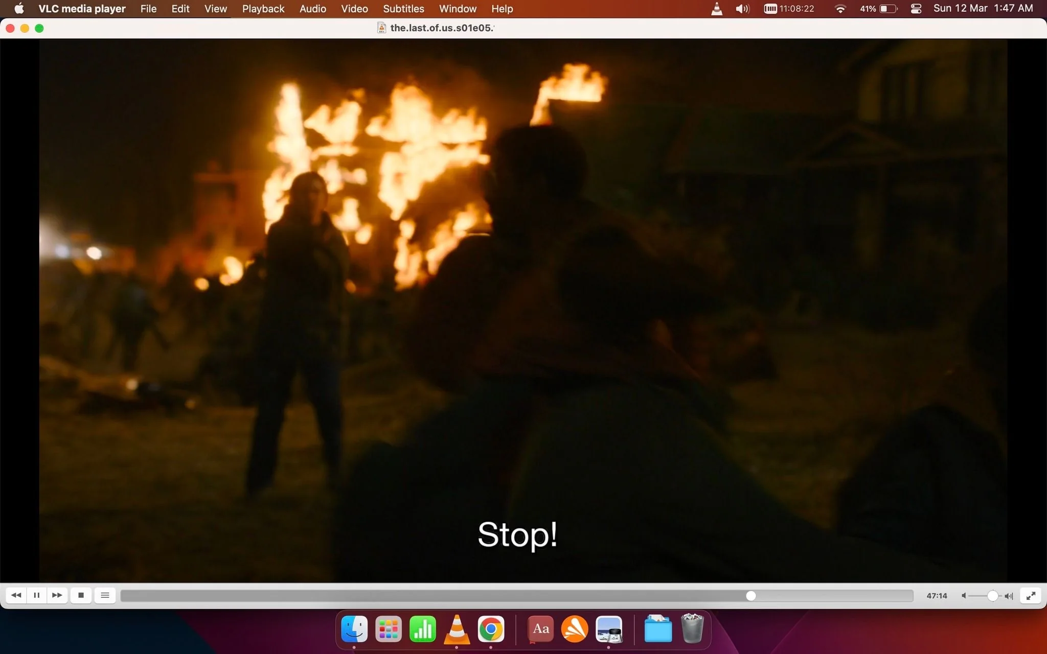 The image is a video frame from the VLC media player, showing a scene from "The Last of Us" series, specifically from episode 5 of the first season. The scene is set at night and depicts a chaotic atmosphere with a large fire blazing in the background, illuminating the area with intense orange light. People are visible, silhouetted against the flames, suggesting a sense of urgency and panic. A person is in the foreground, and their body language indicates movement, possibly in response to the chaos around them. The subtitle at the bottom reads “Stop!” which adds to the tension of the scene. The setting appears to be outdoors, possibly in a residential neighborhood, with houses partially visible amidst the chaos. The overall mood conveyed is one of urgency and disorder, with dramatic lighting enhancing the visual impact. The VLC interface is visible at the top and bottom, showing standard playback controls and the file name of the media being played.