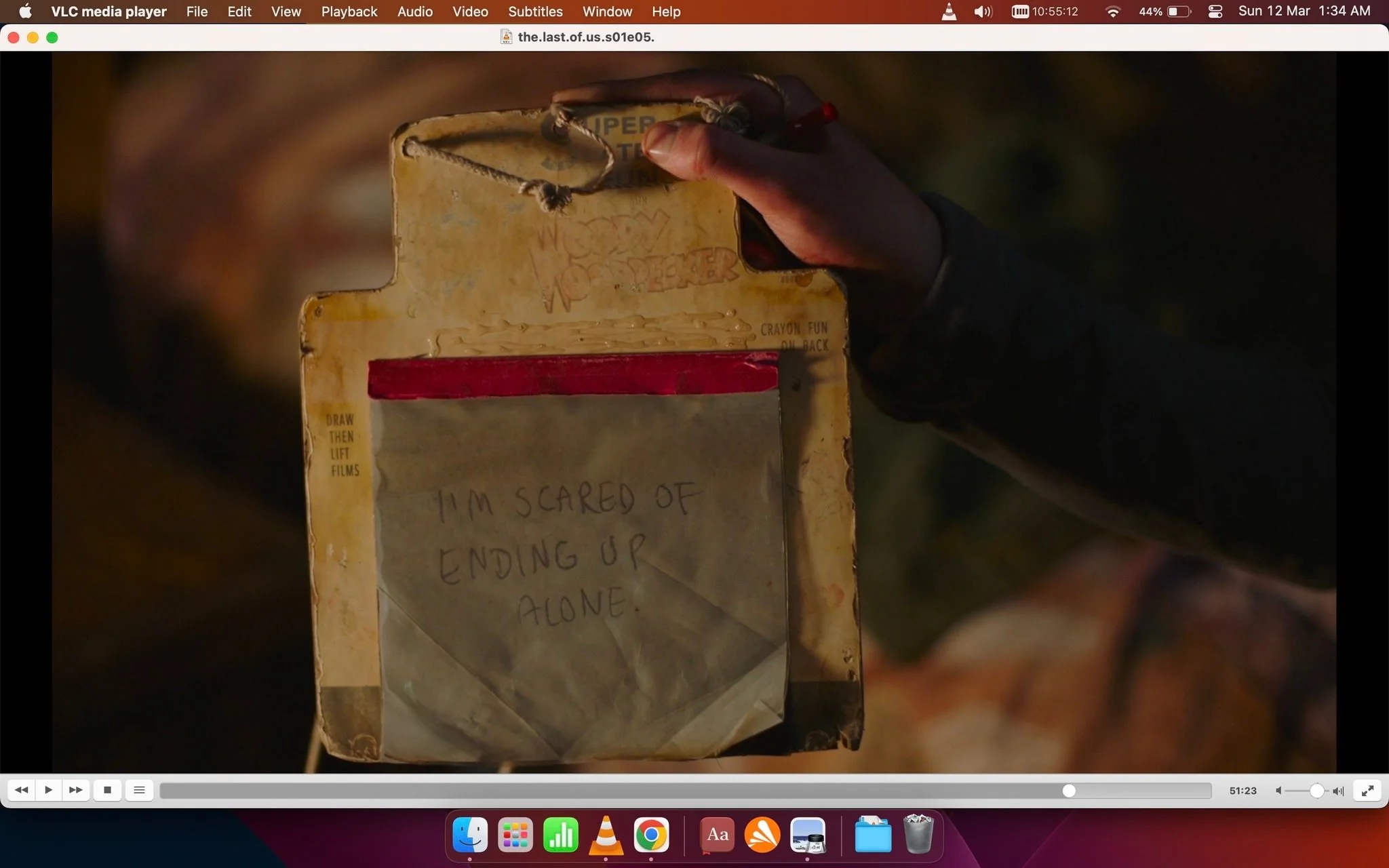 The image is a screenshot from the VLC media player displaying an episode titled "the.last.of.us.s01e05.1080p.web.h264-cakes[eztv.re].mkv," indicating it is from the series "The Last of Us." The scene shows a hand holding a pad with a piece of paper attached. The paper has a handwritten message: "I'M SCARED OF ENDING UP ALONE," suggesting a moment of vulnerability or fear. The pad appears worn and slightly damaged, hinting at a post-apocalyptic or survival setting, consistent with the show's themes. The lighting is warm, creating a somber or reflective mood. The hand holding the pad is partially visible, and the background is blurred, focusing attention on the message. The pad has some printed text, including "DRAW THEN LIFT FILMS" and "CRAYON FUN ON BACK," indicating it might be a child's drawing toy repurposed for communication. The image captures a poignant and emotional moment in the narrative.