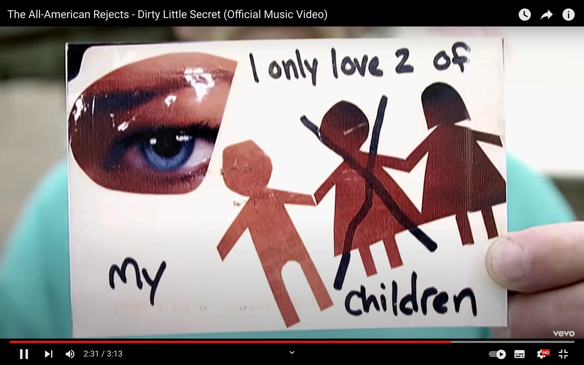 The image is a frame from The All-American Rejects' official music video for the song "Dirty Little Secret," published by Vevo on YouTube. In the frame, a hand holds a card with a collage-like design. The card features a close-up image of a blue eye on the left side and cutout figures of three children on the right. The text on the card reads, "I only love 2 of my children," with the figure of one child crossed out with a black marker, emphasizing the "dirty little secret" theme of the song. The overall color scheme is a mix of earthy tones and the vibrant blue of the eye. The setting is unclear, as the focus is on the card itself. The composition uses a simple, straightforward layout to convey the message effectively. The video captures the concept of hidden truths and personal confessions, aligning with the lyrics and themes of the song.