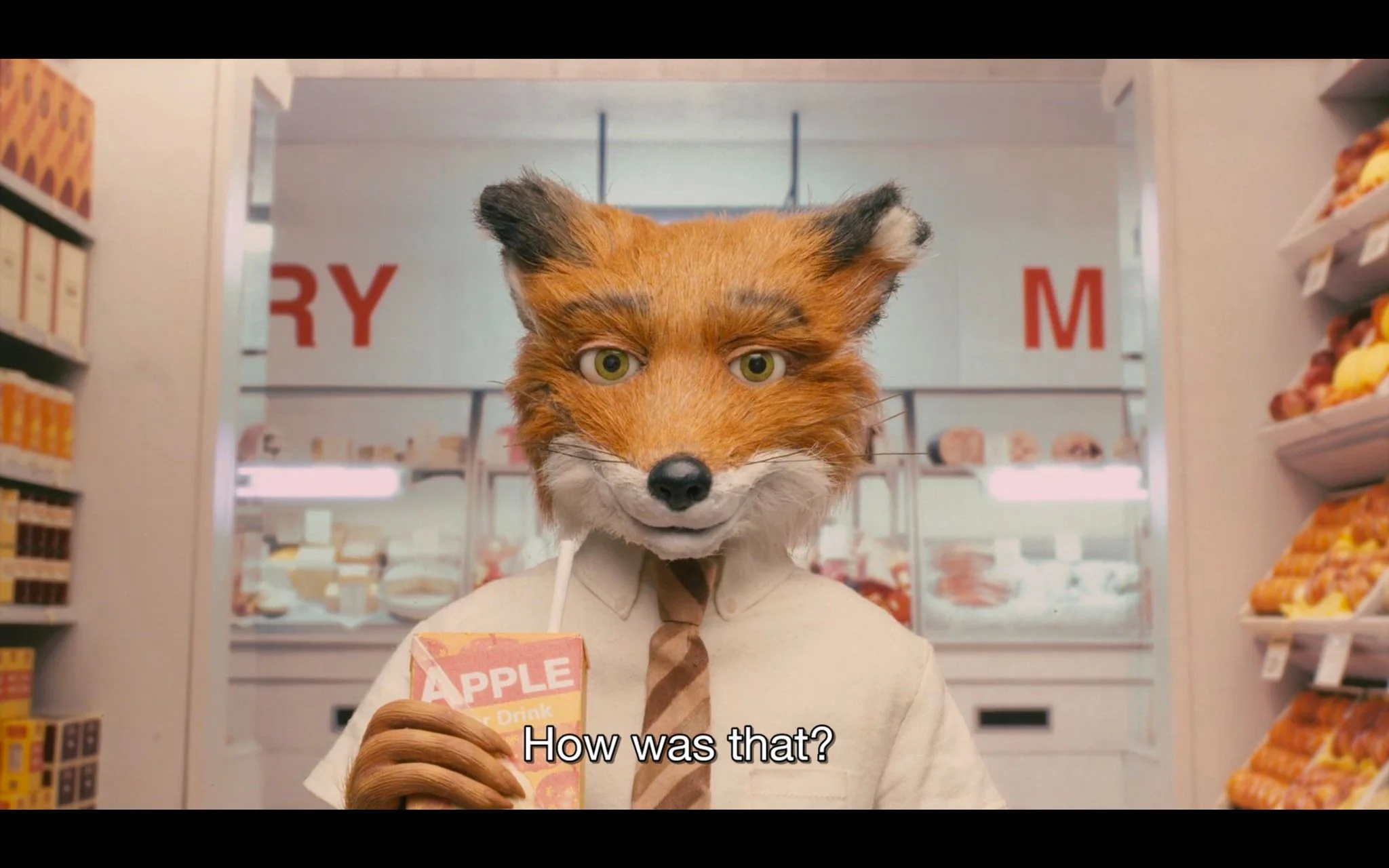 In this image, a character from "Fantastic Mr. Fox" is depicted standing in a supermarket aisle. The character, a fox, is wearing a white shirt with a striped tie, holding a juice box labeled "APPLE Drink" with a straw. The setting is vibrant with a warm and colorful palette typical of stop-motion animation, creating a whimsical and inviting atmosphere. The fox has expressive eyes and a slight smile, adding a playful and curious mood to the scene.
In the background, the shelves are stocked with various products, indicating a grocery store environment. The lighting is bright and even, highlighting the detailed textures of the character's fur and clothing. Subtitles at the bottom read, "How was that?" which suggests a conversational moment, possibly indicating a question or interaction with another character.
- Captions / subtitles: "How was that?"