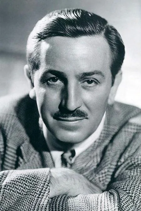 Walt Disney is depicted in this classic black and white portrait. The image captures him in a formal setting, likely a studio, given the controlled lighting and posed composition. Walt Disney is portrayed with a slight, confident smile, looking directly at the camera. His hair is neatly combed back, and he sports a well-groomed mustache. He is dressed in a checkered jacket, a white shirt, and a tie, exuding a professional demeanor. The lighting highlights his facial features, creating a sharp contrast with the background, which is softly out of focus. His posture suggests ease and authority, reflective of his status as a prominent figure in the entertainment industry. The photograph is a testament to his enduring legacy, capturing not just his likeness but the charisma that defined his persona.