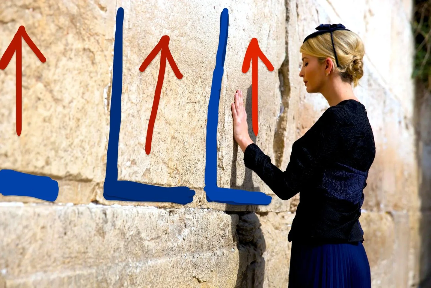Ivanka is depicted standing beside a large, ancient stone wall. She is dressed elegantly in a dark outfit, wearing a black blouse and a matching pleated skirt. Her blonde hair is styled neatly into an updo, adorned with a black headband featuring a bow. Ivanka's posture is respectful and contemplative as she gently places her hand on the wall, her eyes closed, appearing to be in a moment of reflection or prayer. The wall consists of large, weathered stones, suggesting a setting of historical or cultural significance. Red arrows and blue lines are drawn over the wall in a stylized manner, adding a modern, graphic element to the scene. The lighting is bright, indicating a clear day, which casts shadows and highlights the textures of the stones and Ivanka's attire. No additional text or branding is visible in the image.