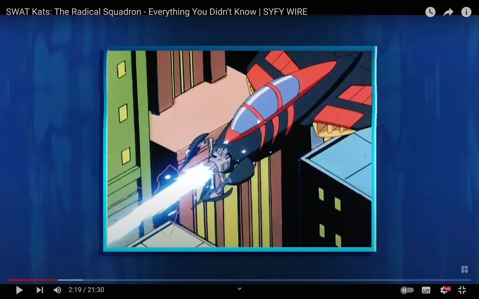 The image is a frame from a YouTube video titled "SWAT Kats: The Radical Squadron - Everything You Didn’t Know | SYFY WIRE." It features an animated scene from the show "SWAT Kats: The Radical Squadron." In the foreground, there is a sleek, red and black jet flying through a cityscape. The jet is depicted shooting a bright beam of light or energy from its nose, suggesting an action-packed moment typical of the show's adventure and combat themes. The buildings are stylized with simplistic, bold colors, typical of 1990s animation. The jet's design is futuristic with a streamlined shape and distinct red markings, reflecting the show's focus on high-tech gadgets and machinery. The animation style is vibrant and dynamic, capturing the essence of the action genre. The video is published by SYFY on YouTube, and its content likely explores interesting facts or behind-the-scenes details about the show.