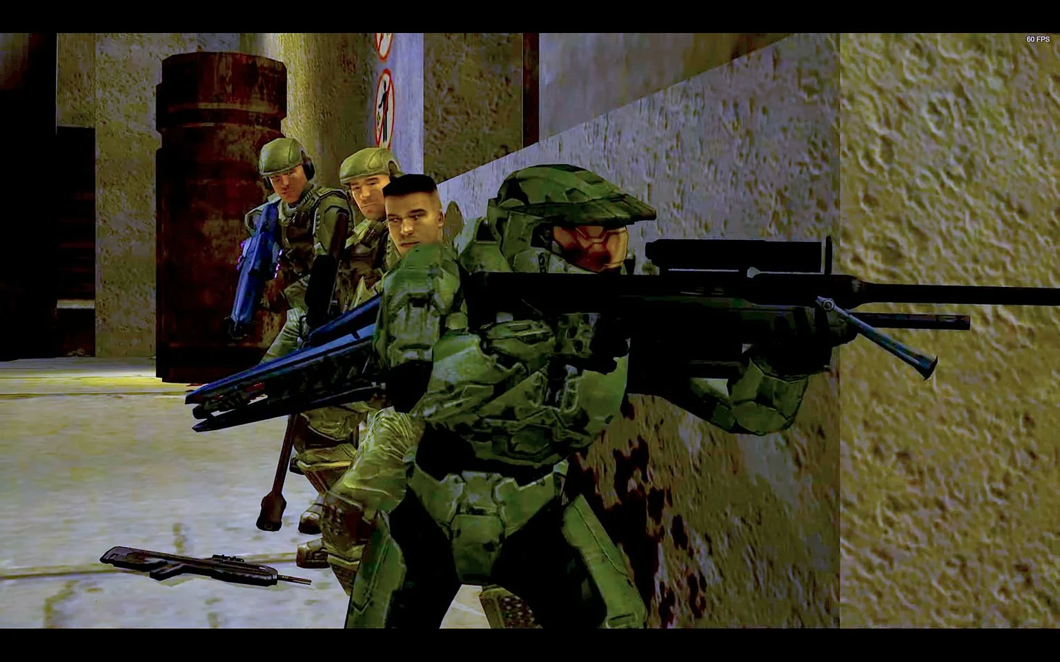 This image is a screenshot from a video game, specifically "Halo." It features a group of characters in a military setting, poised for action along a textured wall. The central figure is wearing a green armored suit, a characteristic outfit of the game's protagonist, Master Chief. He is holding a large, futuristic-looking weapon and appears to be leading the group. Three soldiers, dressed in camouflage uniforms and helmets, are seen behind him, each holding weapons and prepared for combat. The scene is set in a dimly lit, industrial environment with metal barrels and prohibition signs visible in the background, adding to the tense, strategic atmosphere. The lighting emphasizes the details on the characters' armor and weapons, suggesting a moment of anticipation before engagement. The visual style is typical of early 2000s video game graphics, with sharp edges and vibrant colors.