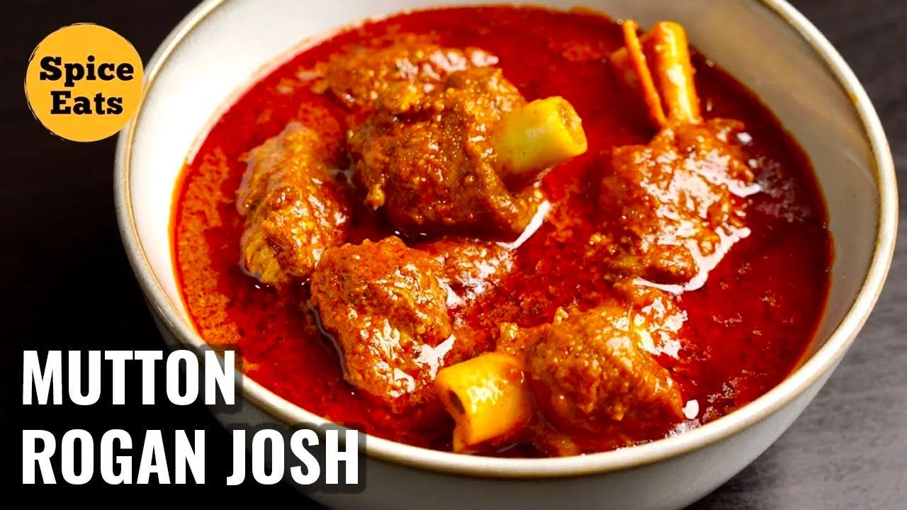 The image displays a bowl filled with Mutton Rogan Josh, a popular Indian curry dish known for its rich, aromatic flavors. The dish is presented in a light-colored bowl, emphasizing the vibrant red color of the curry, which is characteristic of this traditional meal. The surface of the curry is slightly glossy, suggesting a rich, well-cooked sauce. Several pieces of mutton with bone are visible, submerged in the thick, spicy gravy. The image evokes a sense of warmth and indulgence, likely appealing to those interested in hearty, flavorful cuisine.
In the top left corner, there is an orange circular logo with the text "Spice Eats," indicating the name of the channel or brand associated with the dish. The bottom left corner prominently features the title "MUTTON ROGAN JOSH" in bold white letters against a black background. This composition suggests the image might be part of a cooking series or recipe guide from Spice Eats, focusing on this particular dish. The overall presentation is designed to attract viewers interested in cooking or exploring new recipes.