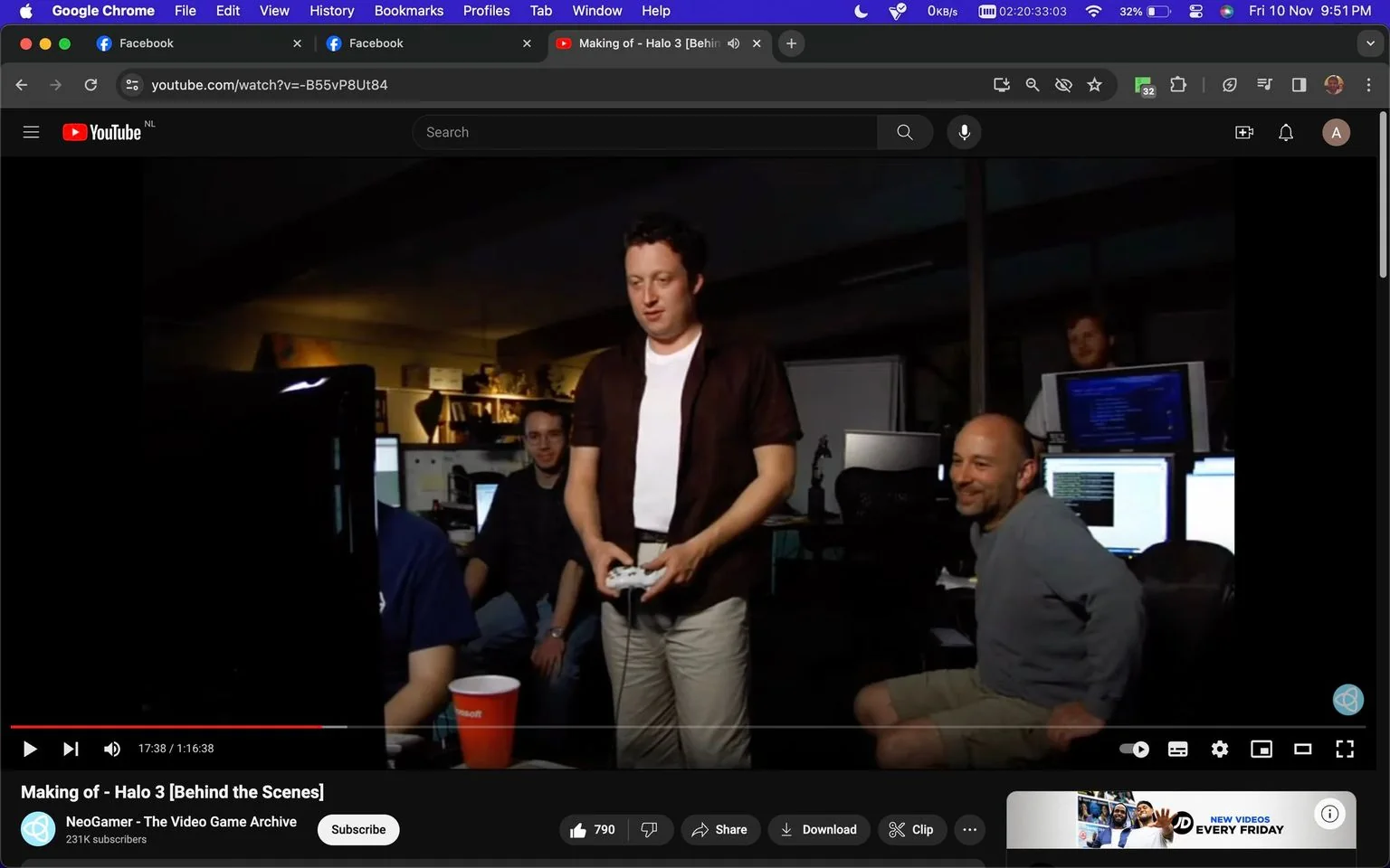 1) Rich description: The image shows a behind-the-scenes view from the making of "Halo 3," a popular video game. The setting is a dimly lit office environment where several individuals are gathered around computer monitors. One person is standing in the center, holding a game controller, wearing a white t-shirt and a dark short-sleeved shirt over it. To his right, another person is seated, smiling, and wearing a casual gray long-sleeve shirt with shorts. There are several computer monitors visible, with one displaying a blue screen filled with code, indicating a development environment. A red cup with the Microsoft logo is prominently placed on a desk, highlighting the connection to the game’s publisher. The atmosphere appears relaxed yet focused, capturing a genuine moment of developers interacting with their work. Ambient lighting and cluttered desks contribute to an authentic depiction of a busy game development studio.
2) On-screen text block:
- Title: "Making of - Halo 3 [Behind the Scenes]"
- Channel / profile: "NeoGamer - The Video Game Archive"
- Site / app: "YouTube"