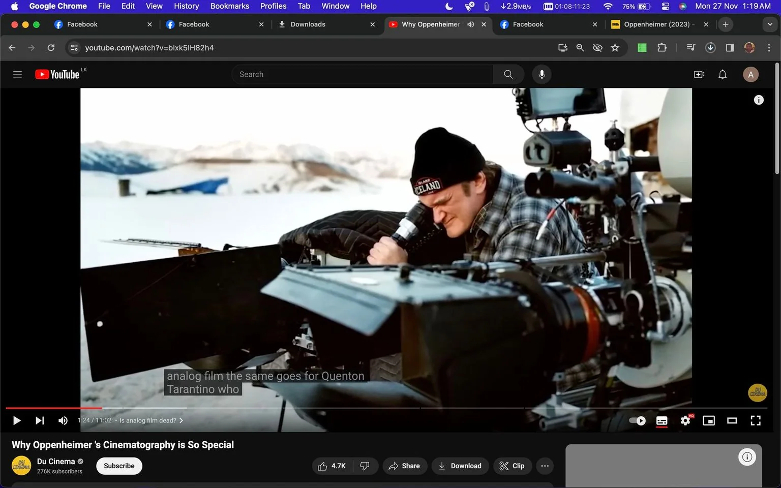 In this YouTube screenshot, the title of the video is "Why Oppenheimer's Cinematography is So Special," and it is hosted on the "Du Cinema" channel. The scene captures an outdoor filming setup in a snowy environment. The main focus is a person identified as Quentin, who is deeply engaged in operating a large piece of camera equipment. He is wearing a plaid shirt and a black beanie with visible text that reads “ICELAND,” suggesting cold weather. The camera equipment is complex, featuring multiple lenses and components, indicating a professional filming scenario. The background shows a snowy landscape with distant mountains, adding to the cinematic atmosphere. The caption on the screen discusses analog film and mentions "Quentin Tarantino," suggesting a conversation about filmmaking techniques. The lighting is natural, providing a clear and bright view of the scene.
