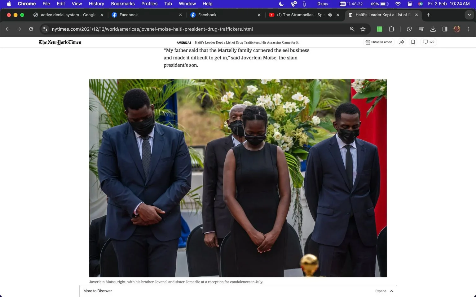 The image is a screenshot from an article on the New York Times website. It shows a solemn scene at a memorial reception, likely taking place outdoors given the presence of plants and flowers in the background. In the foreground are three individuals, identified as Joverlein Moïse, his brother Jovenel, and sister Jomarlie, all wearing formal black attire. They are standing with heads bowed, possibly in mourning or reflection, which conveys a somber and respectful mood. The two men are wearing suits with ties, while the woman is in a simple black dress. All three individuals are masked, adhering to health and safety measures. Behind them, a floral arrangement adds a touch of color and life to the scene, with greenery and white flowers. The setting appears to be a formal occasion, likely related to the aftermath of a significant event involving their family. The image is part of an article discussing political and familial issues, as indicated by the captions and text surrounding the image.