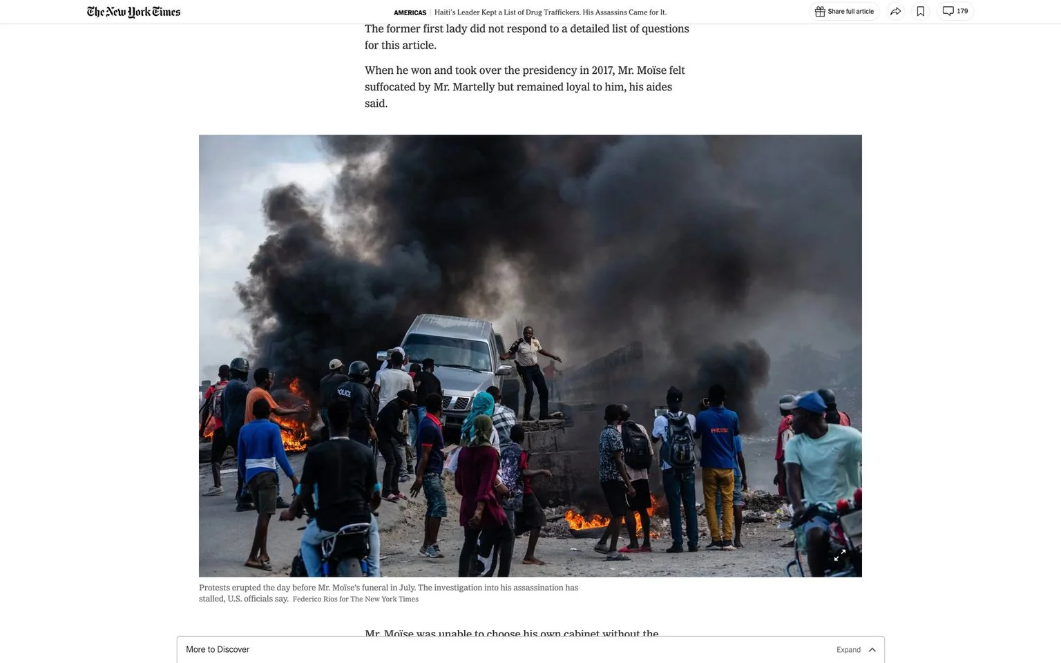 The image depicts a chaotic and tense scene during a protest. It is a photograph published in The New York Times, capturing an event in Haiti related to the assassination of Mr. Moïse. In the foreground, a group of people are gathered around a burning object on the street, with thick, black smoke billowing into the sky. The crowd appears agitated; some individuals are wearing helmets, and one person is standing on a vehicle in a defiant pose. Police officers are visible among the protesters, trying to manage the situation. The atmosphere is charged with tension, highlighted by the dark smoke and the bright flames. The sky is overcast, adding to the somber mood of the scene. This photo encapsulates the unrest and turmoil following the assassination, as noted in the accompanying caption describing how protests erupted the day before Mr. Moïse’s funeral. Federico Rios is credited with capturing this impactful image.