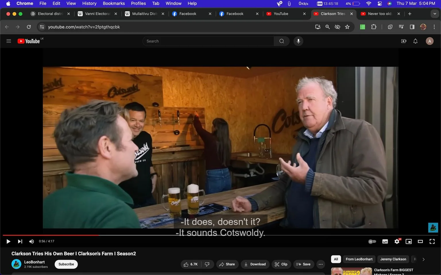 The image is a screenshot from a YouTube video titled "Clarkson Tries His Own Beer | Clarkson's Farm | Season2," published on the channel LeoBonhart. The scene takes place indoors at a bar setting. Jeremy Clarkson is seen on the right, engaging in conversation with two others. He is wearing a jacket over a sweater, typical of his casual style, and appears to be animatedly discussing something, gesturing with his hand.
In the background, a person is pouring drinks, with visible branding reading "Cotswold Brew Co" on the wooden wall and beer taps. Two mugs of beer with foam are set on the bar counter, suggesting a brewery or tasting setting. The lighting is warm, providing a cozy atmosphere. The people are casually dressed, contributing to the laid-back vibe of the scene. Subtitles captured in the screenshot read, "- It does, doesn't it? - It sounds Cotswoldy," indicating a focus on the local or regional branding of the beer.