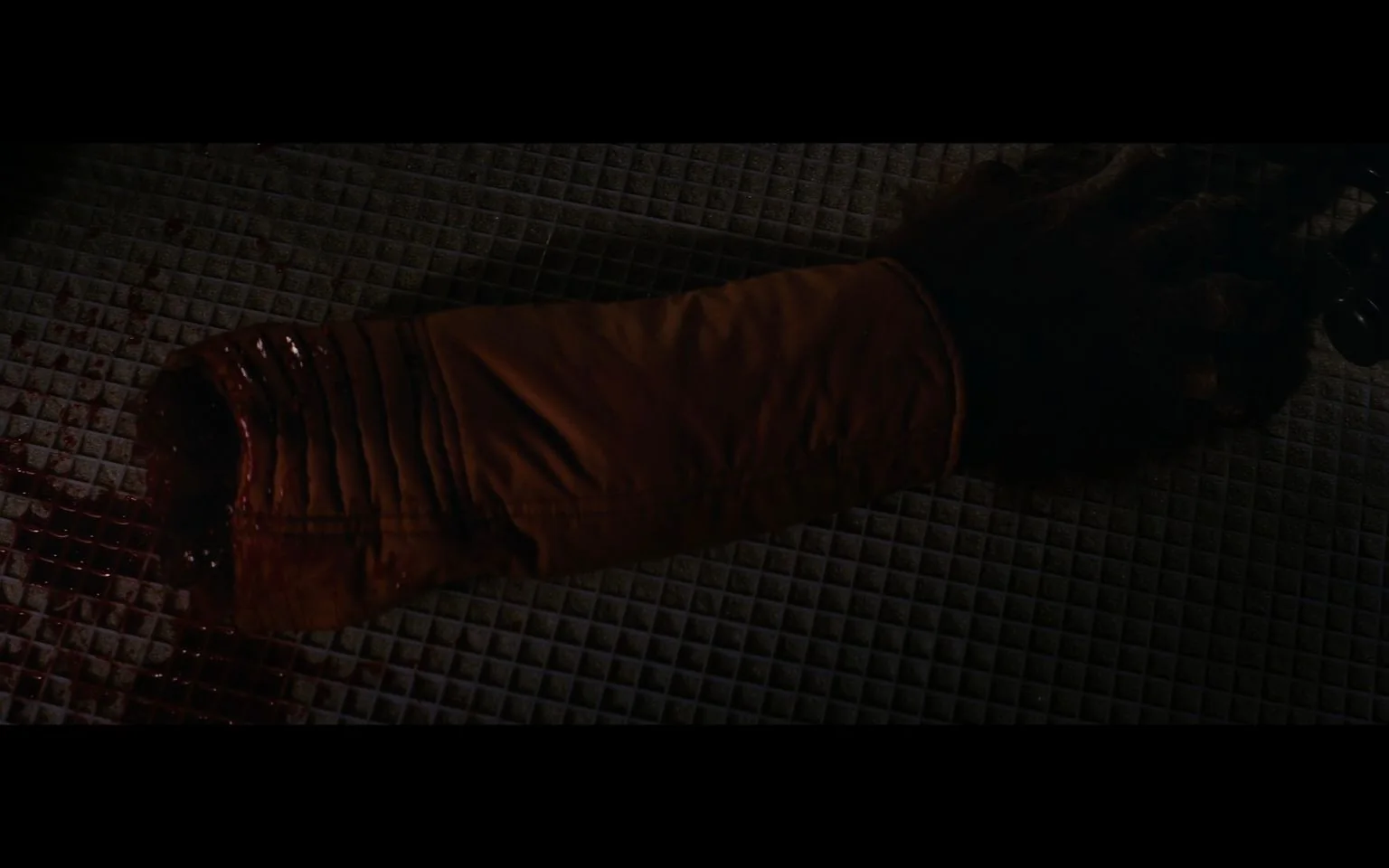 The image is a dramatic and dark scene from "Star Wars." It captures a severed arm, clad in an orange sleeve, lying on a grid-patterned floor. The arm appears to be covered in fur, suggesting it may belong to a non-human character from the "Star Wars" universe. Blood is visible near the severed end of the arm, adding to the intensity of the scene. The lighting is dim, emphasizing the somber and dramatic mood typical of many action-packed moments in "Star Wars" films. The choice of costume and special effects reflects the film’s commitment to detailed and immersive storytelling, characteristic of the "Star Wars" series. The setting appears to be indoors, possibly within a spaceship or a space station, enhancing the science fiction theme of the franchise. The overall composition is designed to evoke a strong emotional response, drawing viewers deeper into the narrative, highlighting the stakes and conflicts faced by the characters in this iconic series.