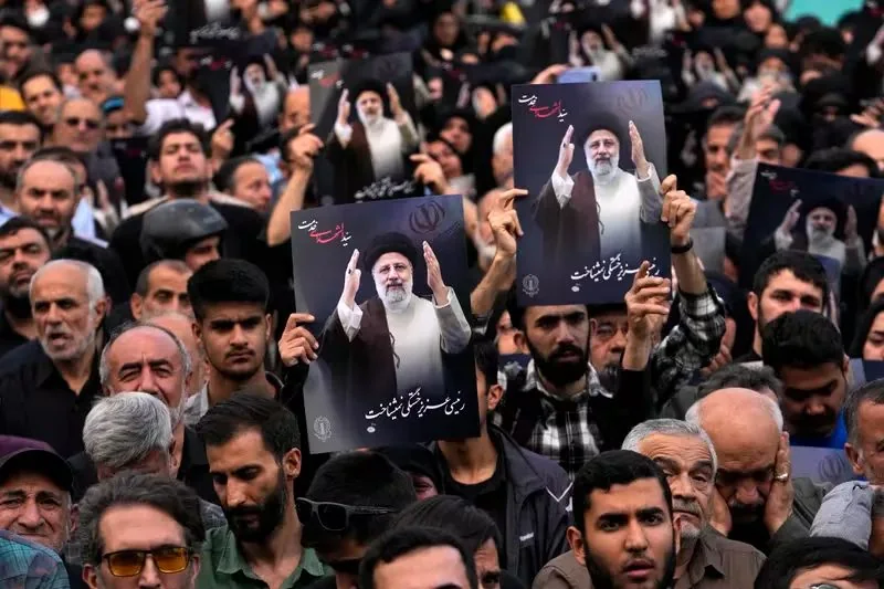 In this image, a large crowd is gathered outdoors during the daytime, participating in a demonstration. The crowd is densely packed, with many individuals holding up posters showing a man dressed in traditional attire, including a black turban and robe, suggesting a religious or political figure of significance. The mood appears intense and focused, as many in the crowd hold up the posters high above their heads, suggesting a show of support or protest.
The posters prominently display the man's image, who is gesturing with raised hands, and contain text in Persian script, including the phrase "رئیس جمهور رئیسی," which translates to "President Raisi." The background is filled with numerous individuals, indicating a large-scale event. This image is likely capturing a moment of political or social significance, reflecting the sentiments of the gathered crowd. The lighting is natural, contributing to the clarity of the scene, and the overall composition centers on the posters being prominently displayed.