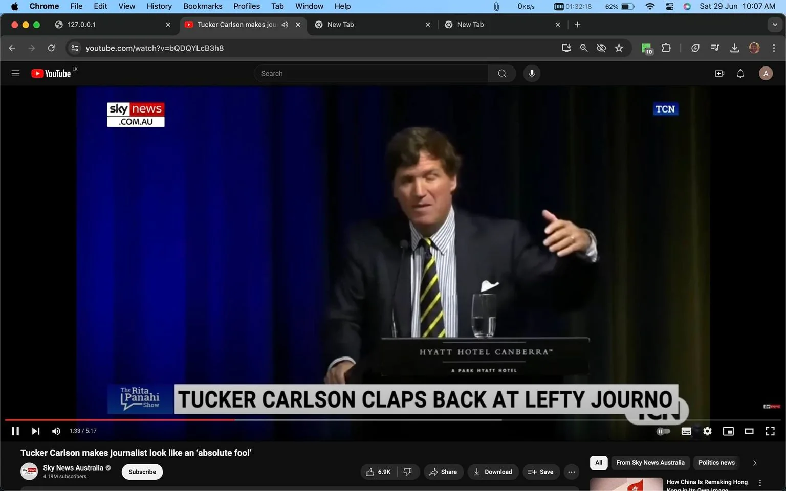 1) Rich description:
The image is a screenshot from a YouTube video featuring a man identified through a hint as Tucker Carlson. He is giving a speech or presentation at the Hyatt Hotel Canberra, as indicated by the text on the podium. The setting appears to be a formal event or conference, with a dark blue curtain in the background suggesting an indoor venue. Tucker Carlson is wearing a dark suit with a white shirt and a striped tie, projecting a professional appearance. His posture suggests he is gesturing, likely emphasizing a point during his speech. The lighting is focused on him as he stands behind a microphone, giving him prominence in the scene. The video is titled "Tucker Carlson makes journalist look like an ‘absolute fool’," and is hosted on the Sky News Australia channel. The lower third of the screen displays the text "TUCKER CARLSON CLAPS BACK AT LEFTY JOURNO," implying a confrontational or critical narrative. The screenshot captures a moment from "The Rita Panahi Show," as indicated in the overlay text on the screen.
2) On-screen text block:
- Title: "Tucker Carlson makes journalist look like an ‘absolute fool’"
- Channel / profile: "Sky News Australia"
- Site / app: "YouTube"