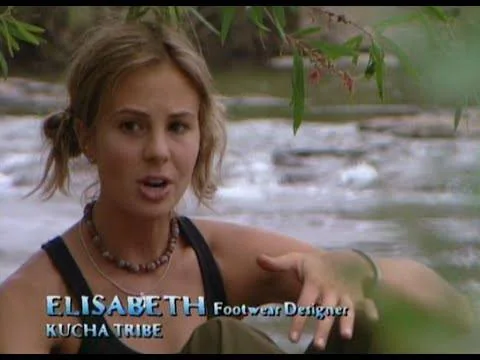 Elisabeth Hasselbeck is featured in this scene from the reality show "Survivor." She is seated outdoors near a body of water, suggesting a natural, serene setting, likely in a tropical location. The background consists of flowing water and lush greenery, contributing to a peaceful and natural atmosphere. Elisabeth is dressed casually in a black tank top and wears a beaded necklace, indicative of the show's rugged, survival-themed context. Her expression appears engaged, perhaps as she shares her thoughts or experiences as part of the Kucha Tribe. The on-screen text identifies her as a "Footwear Designer" and a member of the "Kucha Tribe," providing context about her role and background on the show. The lighting is natural, enhancing the authenticity of the setting. This image captures a moment of personal reflection or conversation, typical of the interview segments in "Survivor."
- Title: "ELISABETH"
- Key OCR Lines: "Footwear Designer", "Kucha Tribe"