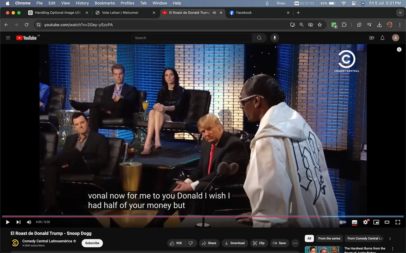 The image is a screenshot from a YouTube video titled "El Roast de Donald Trump - Snoop Dogg," featured on the Comedy Central Latinoamérica channel. It shows a scene from a comedy roast event. In the foreground, a figure identified as Snoop is wearing a white jacket with black lettering on the back, speaking into a microphone. Seated to the right is a person identified as Trump, dressed in a dark suit and red tie, looking towards Snoop.
In the background, other people are seated on stage, including a person identified as Seth, wearing a dark suit, sitting in a relaxed manner. The setting appears to be a studio with a sleek, modern design, featuring textured blue and bronze-colored panels. There's a comedic and lively atmosphere, typical of roast events, with the audience and participants appearing engaged and entertained.
- Title: "El Roast de Donald Trump - Snoop Dogg"
- Channel / profile: "Comedy Central Latinoamérica"
- Site / app: "YouTube"
- Captions / subtitles: "vocal now for me to you Donald I wish I had half of your money but"