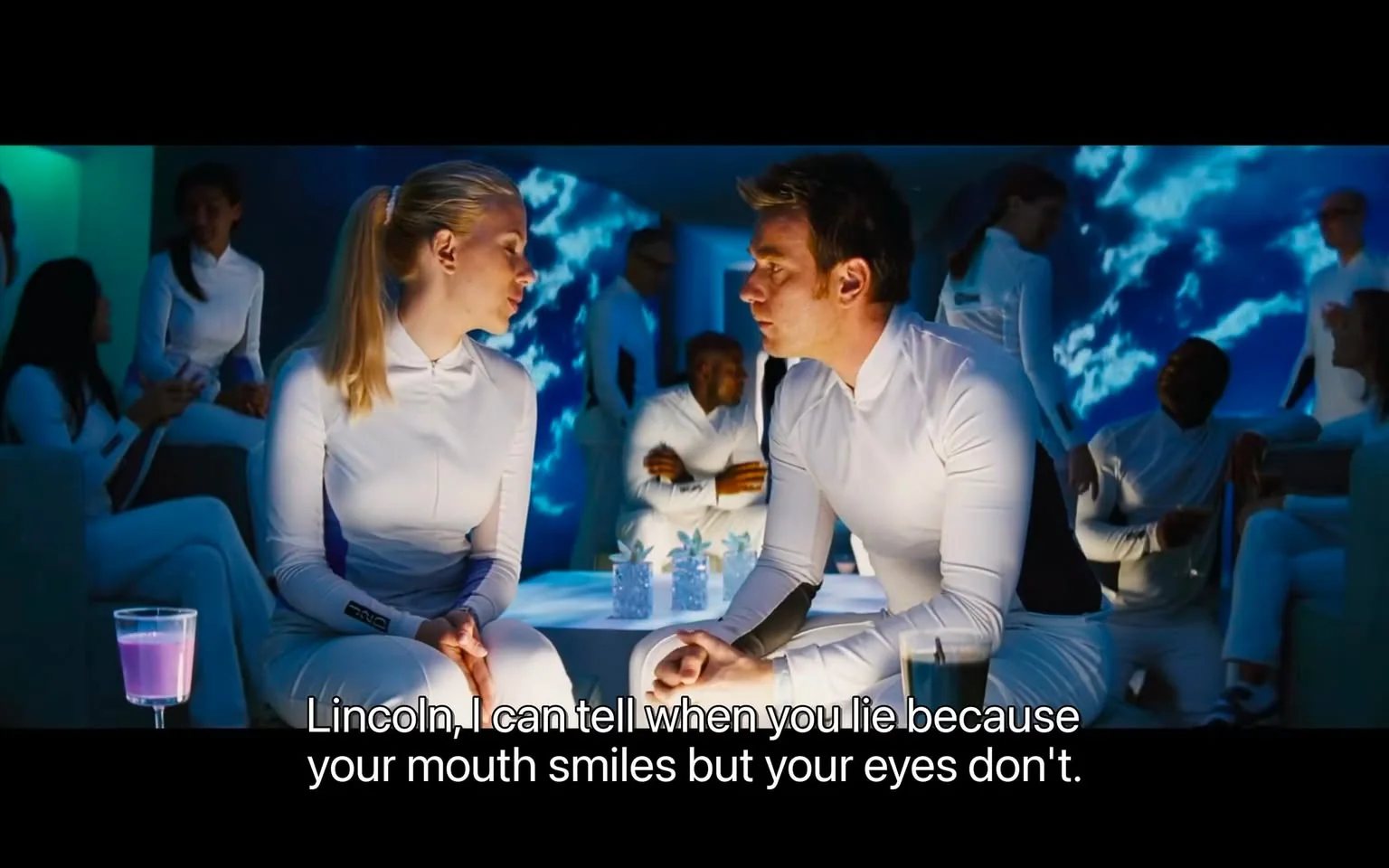 ```
Scarlett Johansson is featured in this scene set in a futuristic-looking indoor environment, characterized by blue ambient lighting and a sleek, modern aesthetic. She is seated on a white bench, engaged in conversation with another character named Lincoln. Both are dressed in matching white outfits, typical of a sci-fi setting, suggesting a uniform or specialized attire linked to the narrative. The background includes other people similarly dressed, indicating a communal or institutional setting. The lighting casts a cool tone, enhancing the sci-fi atmosphere. The scene is tense yet intimate, as Scarlett Johansson's character reveals an ability to discern Lincoln's truthfulness, adding emotional depth to the interaction. The setting is minimalist, with a focus on the characters and their dialogue, as emphasized by the present subtitle.
- Captions / subtitles: "Lincoln, I can tell when you lie because your mouth smiles but your eyes don't."