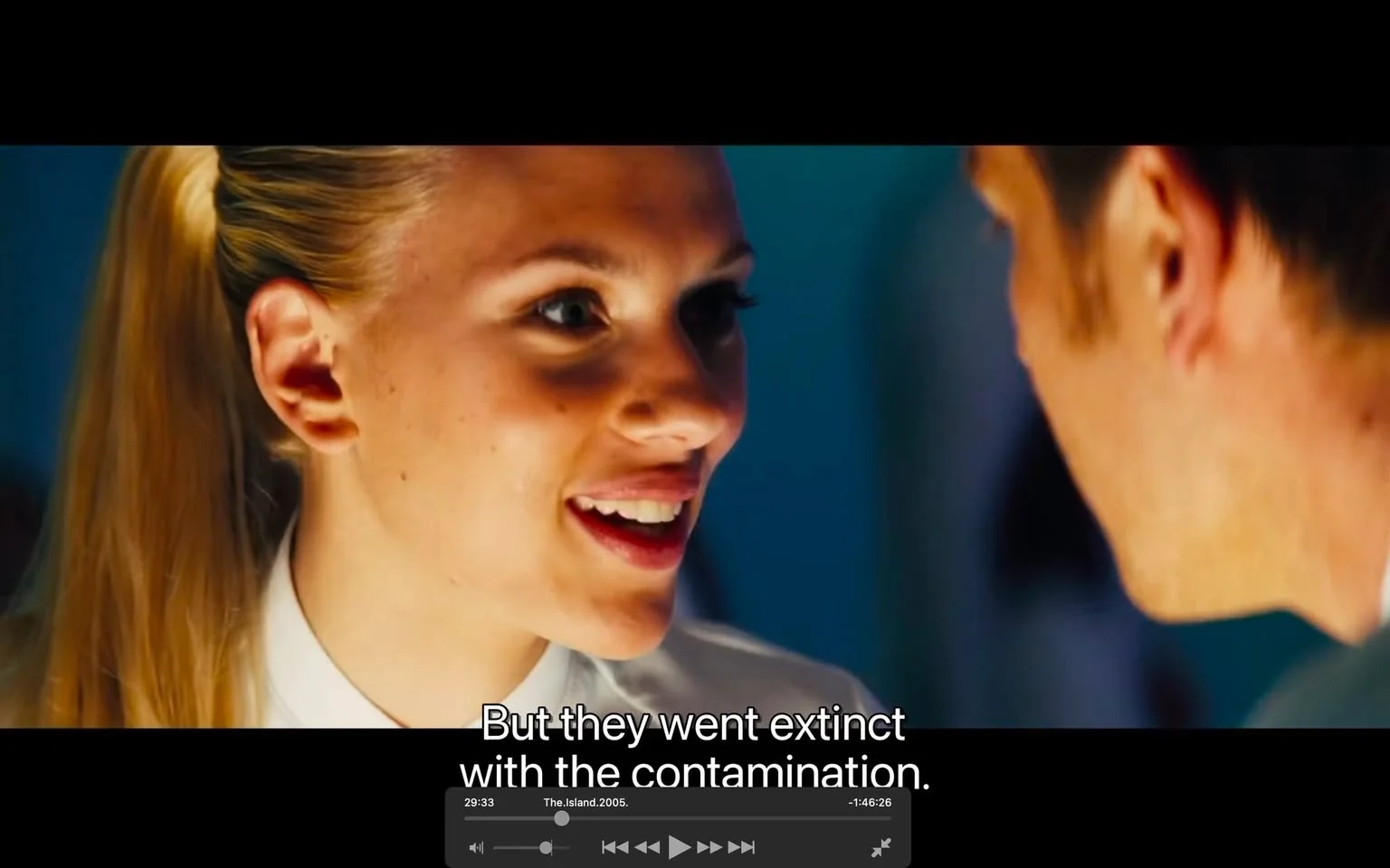 Scarlett Johansson is featured prominently in this video frame from the film "The Island." The scene captures a close-up of her face as she engages in a conversation with another character whose back is slightly turned to the camera. Scarlett Johansson sports a sleek, blonde ponytail and is dressed in a white shirt, suggesting a clean and modern setting. Her expression is animated and lively, indicating that she is deeply engaged in the dialogue. The lighting is bright, highlighting her features and creating a vivid contrast against the blue background. The subtitle reads, "But they went extinct with the contamination," giving context to the conversation's focus on a dystopian or post-apocalyptic theme. The video controls at the bottom indicate the film's title and technical details, such as "The Island.2005.1080p.BluRay.HEVC.DTS.5.1.x265-".
- Captions / subtitles: "But they went extinct with the contamination."