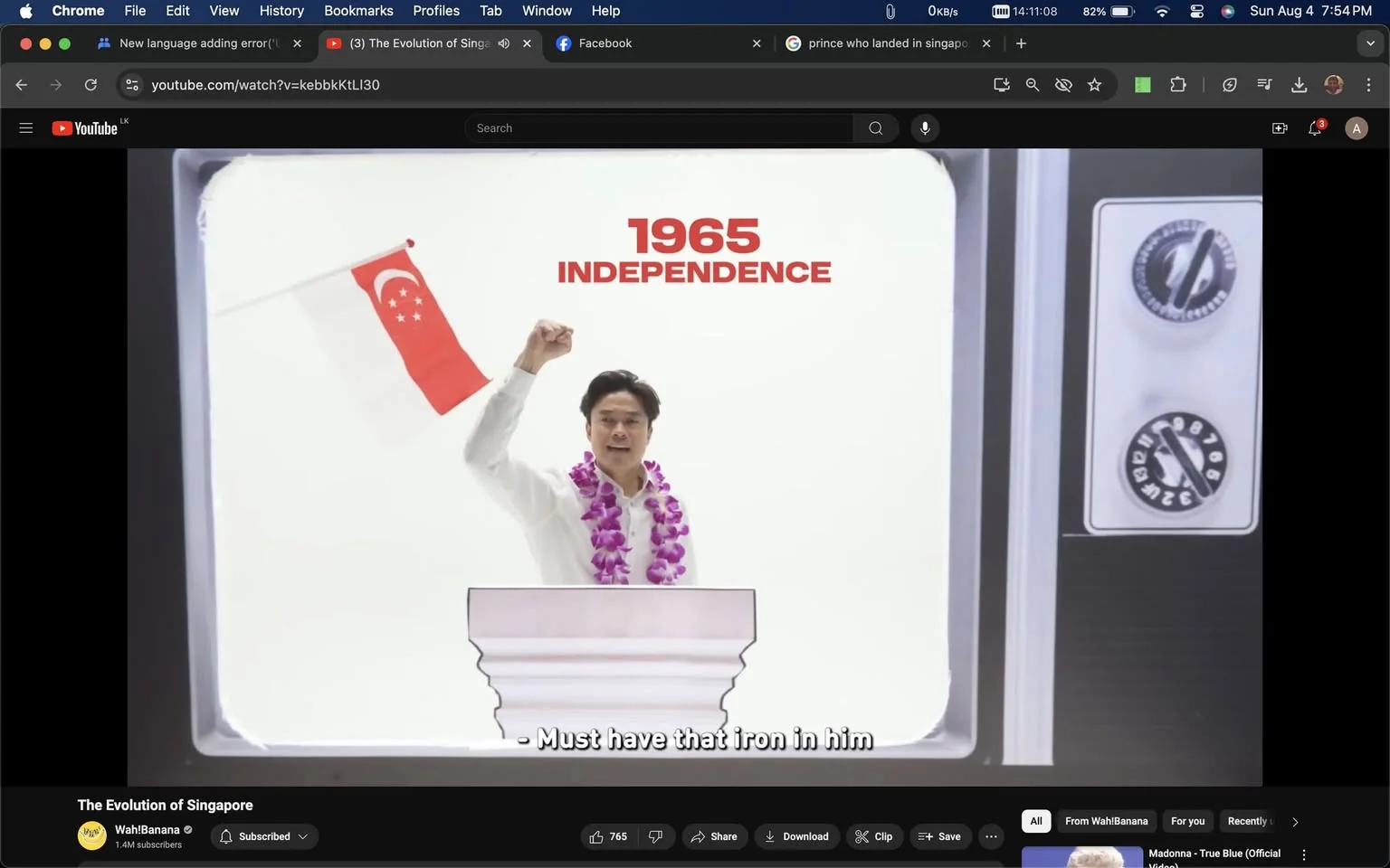 The image is a video frame from a YouTube video titled "The Evolution of Singapore" on the channel Wah!Banana. The scene appears to depict a historical moment from 1965, the year of Singapore’s independence. In the center is a man delivering a speech, standing behind a podium. He is dressed in a white shirt and adorned with a purple flower lei. His right fist is raised in a gesture of triumph or emphasis, symbolizing determination or celebration. In his left hand, he holds a small Singapore flag. The background is minimal, with a stark white backdrop enhancing the focus on the speaker. On the right side of the frame, there are controls resembling those of an old television set, adding a vintage feel to the scene. The text "1965 INDEPENDENCE" is prominently displayed above the speaker's head, marking the historical context. The caption at the bottom reads, "Must have that iron in him," suggesting admiration for the speaker's strength or resilience. The overall mood is one of patriotic celebration and remembrance.
- Title: "The Evolution of Singapore"
- Channel / profile: "Wah!Banana"
- Site / app: "YouTube"
- Captions / subtitles: "Must have that iron in him"