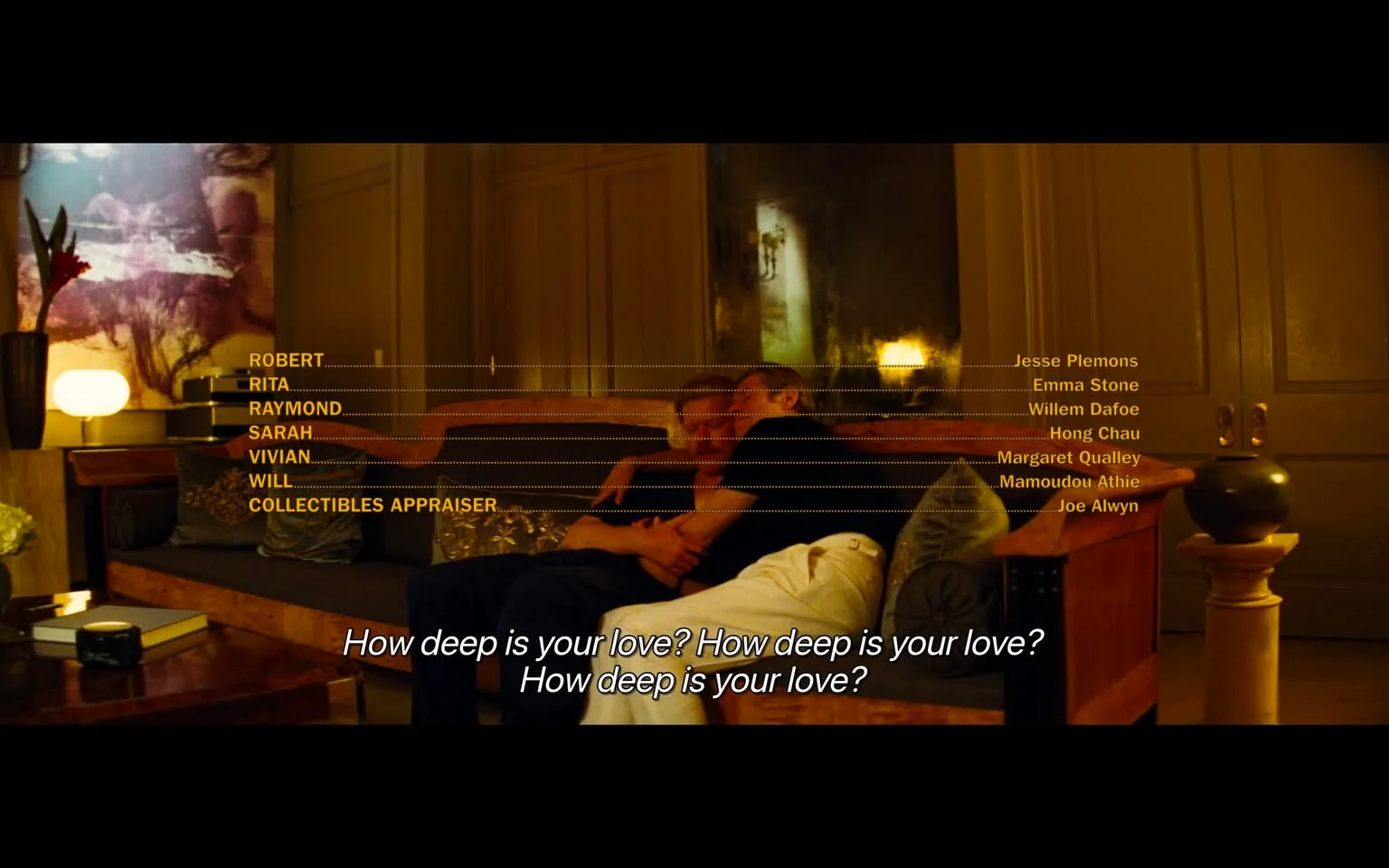 A warm and cozy scene unfolds in what appears to be a well-furnished living room. Two individuals are comfortably seated on a sofa, suggesting an intimate and relaxed atmosphere. The lighting is soft and ambient, casting a gentle glow over the room, which enhances the sense of warmth. The background features large wooden doors and a lamp, adding to the cozy setting. Decorative elements like cushions and a vase with a red flower are visible, contributing to the room's elegant decor.
In the foreground, the text displays names alongside roles, indicating a cast list. The names include Jesse Plemons, Emma Stone, Willem Dafoe, Hong Chau, Margaret Qualley, Mamoudou Athie, and Joe Alwyn. This suggests a connection to a film or television production, possibly involving these individuals.
The scene is accompanied by subtitles reflecting the lyrics of "How Deep Is Your Love?", adding an emotional layer to the visual. The overall mood is intimate and slightly nostalgic, reinforced by the soft lighting and close positioning of the individuals on the sofa. The style of the scene, combined with the textual elements, points towards a narrative moment in a visual medium, likely a film or TV episode.