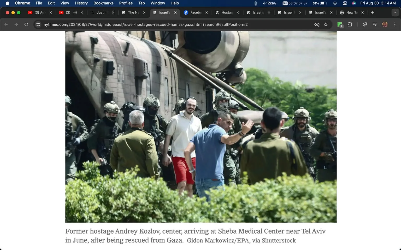 The image depicts a scene of a military operation, centered around a helicopter, with several soldiers and individuals gathered nearby. Andrey Kozlov, identified as a former hostage, is seen in the center of the frame. He is wearing a white shirt and red shorts, walking alongside military personnel. The soldiers are dressed in military fatigues with helmets and gear, conveying a sense of urgency and security.
In the background, the tail section of a large helicopter is visible, hinting at a recent rescue operation. The setting appears to be outdoors, with some greenery visible in the foreground, suggesting a location near an airfield or a secured facility. The atmosphere is tense yet relieved, as Kozlov appears calm and possibly relieved as he is being escorted by the military personnel.
The image is a still from a news article on the New York Times website, titled "Israel Hostages Rescued from Hamas Gaza." It captures the moment Kozlov arrives at Sheba Medical Center near Tel Aviv after being rescued from Gaza. The composition emphasizes the successful rescue mission, highlighting the coordinated efforts of the military team involved.