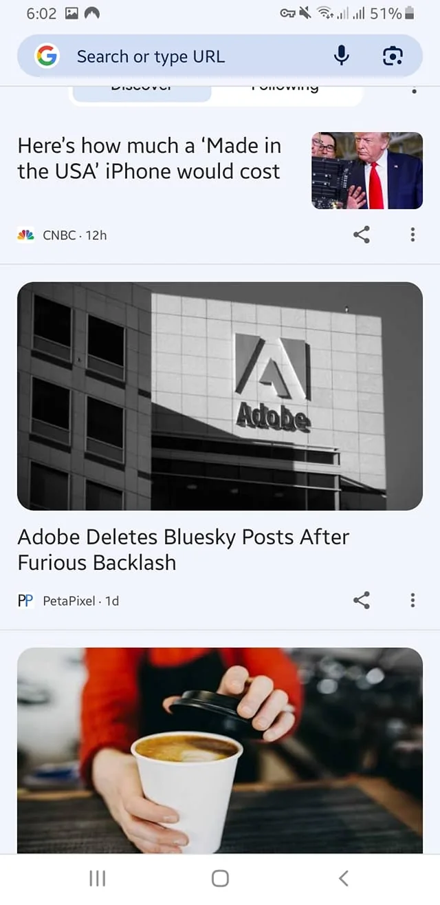 The image displays a mobile screen with a Google search interface. At the top, there is a search bar labeled "Search or type URL" with options for "Discover" and "Following" visible. The time displayed is 6:02, and the battery percentage is at 51%.

The first post features a headline that reads, "Here's how much a ‘Made in the USA’ iPhone would cost," attributed to CNBC and dated 12 hours ago. Next to this headline, there is a small image of a man, but I cannot identify him.

Below that, there is another post with the headline "Adobe Deletes Bluesky Posts After Furious Backlash," credited to PetaPixel and dated 1 day ago. This post includes an image of a building with the Adobe logo prominently displayed. The logo consists of a stylized letter "A" in red, with the word "Adobe" written in a bold, black font beneath it. The building appears to be modern, with a glass facade and a grid-like pattern.

The final post shows a hand holding a white coffee cup with a black lid. The hand is wearing a long-sleeve shirt, possibly red, and the background is slightly blurred, suggesting a café or coffee shop setting. The cup has a circular opening at the top, indicating it contains a beverage, likely coffee.

Overall, the screen captures various articles and images related to technology and lifestyle, with a focus on current news and trends.