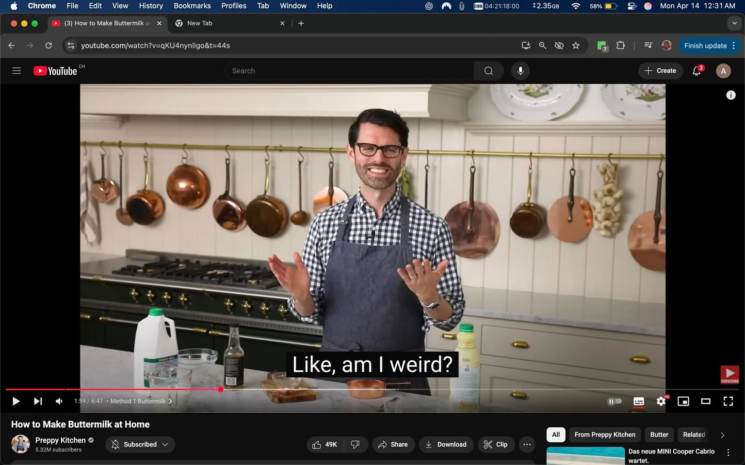 The image features a kitchen setting with a man standing in front of a countertop. He has a friendly expression, smiling while gesturing with his hands. He is wearing a blue apron over a black and white checkered shirt. His hair is dark and neatly styled, and he has glasses. 

On the countertop, there are several items visible: a clear glass bowl, a glass of liquid, and a white plastic container with a green cap, which appears to be a bottle of buttermilk. There is also a small bottle, possibly containing vinegar or another liquid, next to the glass bowl. 

In the background, there is a large, professional-grade stove with a dark green finish and gold knobs. Above the stove, there are several copper pots and pans hanging from a brass rod, adding a rustic touch to the kitchen decor. The walls are painted white, and there are decorative plates displayed on a shelf above the stove.

The overall atmosphere of the kitchen is bright and inviting, with a clean and organized appearance. The man appears to be engaged in a cooking demonstration, likely discussing how to make buttermilk, as indicated by the video title visible at the bottom of the image. The text overlay on the image reads, "Like, am I weird?" suggesting a light-hearted or humorous tone in his presentation. 

No logos or trademarks are prominently displayed in the image, aside from the YouTube branding at the bottom. The setting appears to be a home kitchen or a cooking studio, designed for instructional videos.