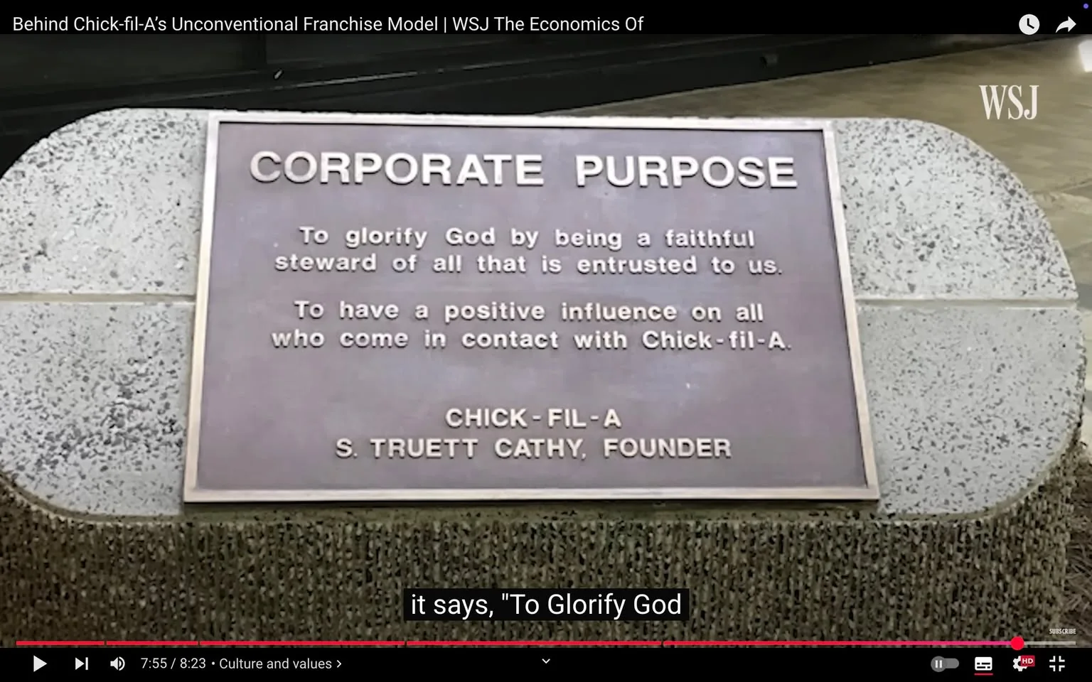 The image features a plaque with the title "CORPORATE PURPOSE" prominently displayed at the top in bold, capital letters. Below the title, there are two main statements:

1. "To glorify God by being a faithful steward of all that is entrusted to us."
2. "To have a positive influence on all who come in contact with Chick-fil-A."

The plaque is attributed to "CHICK-FIL-A" and includes the name "S. TRUETT CATHY, FOUNDER" at the bottom. The text is presented in a clear, legible font, with the first two statements in a slightly smaller size than the title and the brand name.

The plaque appears to be mounted on a textured surface, possibly a wall or a stone structure, which is visible in the background. The overall color scheme of the plaque is a mix of dark and light tones, likely bronze or a similar material, giving it a formal appearance.

The surrounding environment is not fully visible, but the setting appears to be indoors, possibly within a Chick-fil-A restaurant or corporate office, given the context of the plaque. The lighting is soft, suggesting a welcoming atmosphere. There are no people visible in the image, focusing solely on the plaque and its message.