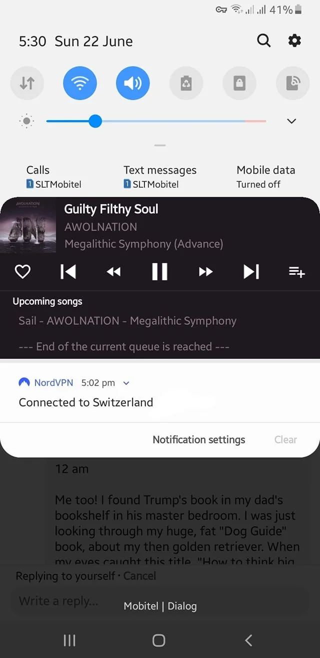 The image displays a smartphone screen with various elements visible. At the top, the time reads "5:30" and the date is "Sun 22 June." The battery level is at 41%, and the mobile network indicator shows a connection to "SLTMobitel." Below this, there are icons for calls, text messages, and mobile data, with the mobile data turned off.

The music player interface is prominent, showing the song "Guilty Filthy Soul" by AWOLNATION from the album "Megalithic Symphony (Advance)." The album artwork features three dark, abstract figures against a backdrop of water or a dark landscape. The player controls include play, pause, and skip buttons, with a queue indicating the next song is "Sail" by the same artist. A message states, "End of the current queue is reached."

At the bottom of the screen, there is a notification from NordVPN, indicating a connection to Switzerland at 5:02 PM. Below this notification, there is a text message thread that begins with a timestamp of "12 am." The message discusses finding a book by Trump in a bookshelf and mentions a "Dog Guide" book.

The overall layout is typical for a smartphone interface, with a clean design and easy navigation elements. The background is a light color, and the text is dark for contrast. There are no visible people, clothing, or facial expressions in this image, as it focuses solely on the smartphone screen and its contents.
