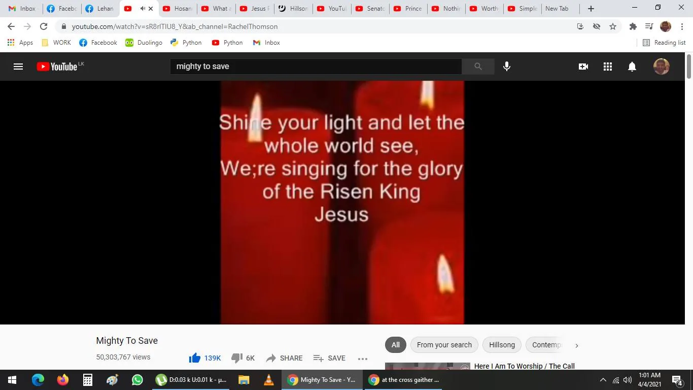 The image is a screenshot from YouTube showing a video titled "Mighty To Save" on the channel "RachelThomson." The video displays lyrics over a background of red candles, creating a warm and serene visual atmosphere. The text on the screen reads: "Shine your light and let the whole world see, We're singing for the glory of the Risen King Jesus." This suggests that the video is likely a lyric video for the worship song "Mighty to Save," which is often associated with themes of faith and worship. The video has amassed over 50 million views, indicating its popularity. Below the video, there are buttons for liking, sharing, and saving the video, reflecting standard YouTube interface features. The surrounding tabs in the browser show a variety of open websites and applications, suggesting that the user is engaged in multiple online activities. The overall tone of the image is reflective and spiritual, enhanced by the imagery of lit candles, which are often associated with worship and contemplation.