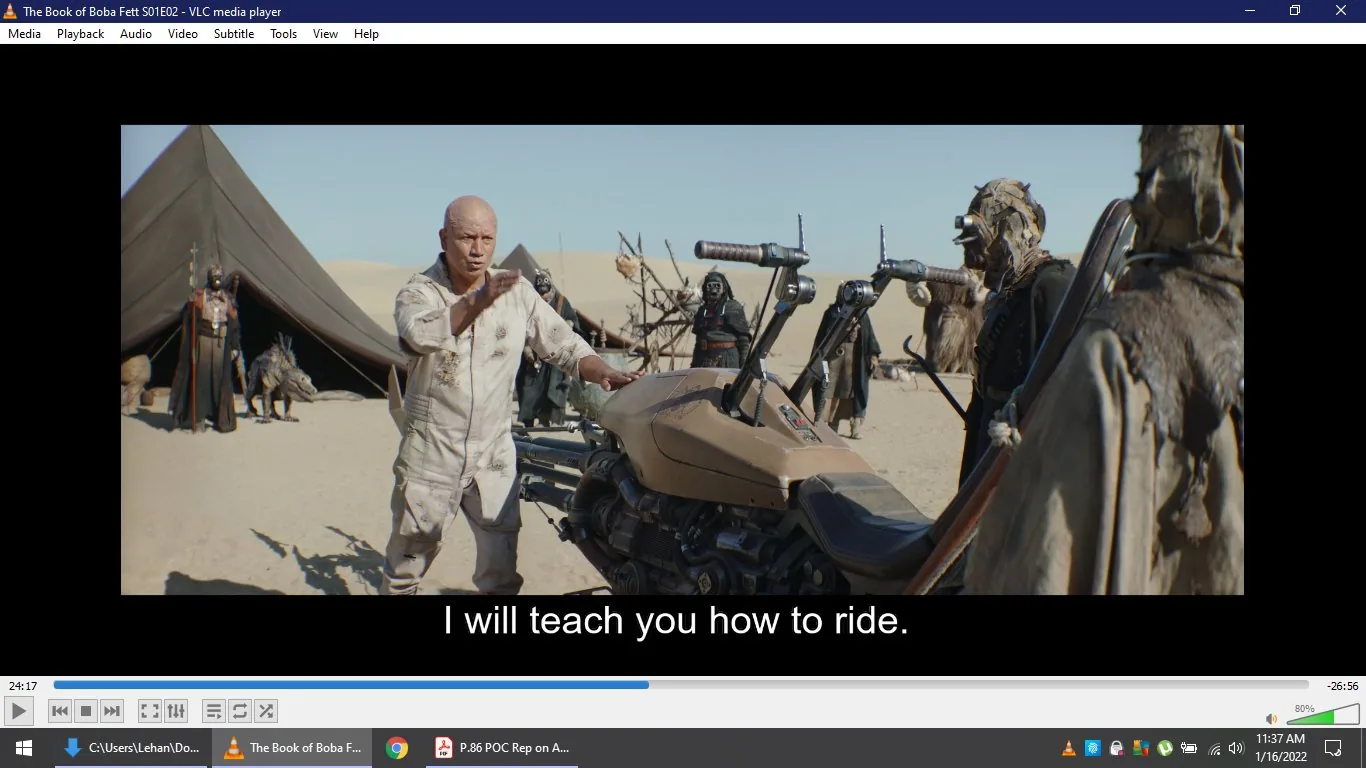 In this scene from "The Book of Boba Fett" S01E02, a character stands in a desert setting, likely on the planet Tatooine. The foreground features a sandy landscape with a large tent in the background, suggesting a nomadic or tribal environment. The main character, who appears to be instructing others, is dressed in a light, rugged outfit suitable for desert conditions, and gestures towards a speeder bike, indicating an intent to teach riding skills. Surrounding him are individuals garbed in robes and masks typical of Tusken Raiders, a group known for their connection to the desert. The lighting is bright, emphasizing the arid climate. The speeder bike, central to the scene, has a sleek, angular design that contrasts with the organic elements around it. This image captures a moment of cultural exchange or skill transfer amidst a blend of technology and tradition.
- Title: "The Book of Boba Fett S01E02"
- Site / app: "VLC media player"
- Captions / subtitles: "I will teach you how to ride."