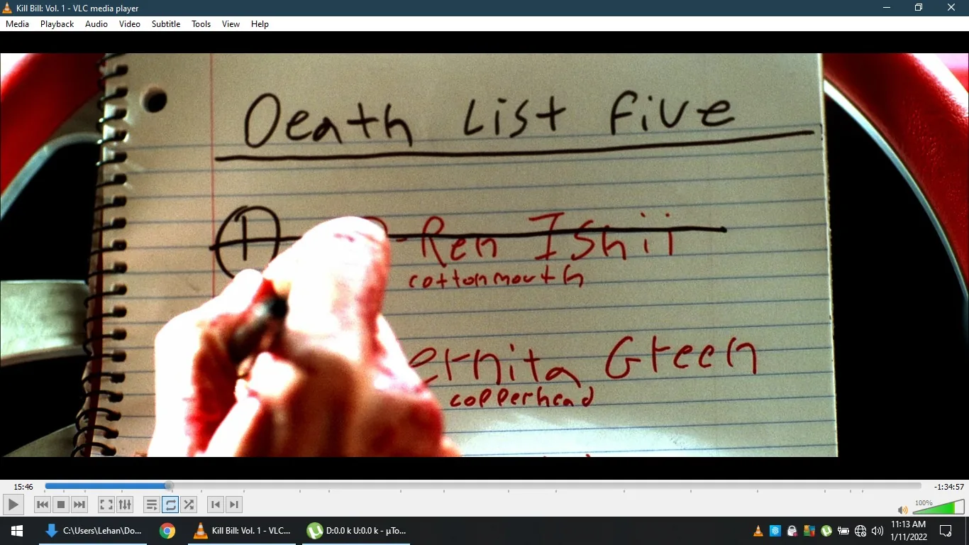 This image is a screenshot from the film "Kill Bill: Vol. 1," as indicated by the title bar of the VLC media player interface. The scene shows a close-up of a handwritten list titled "Death List Five" on a piece of lined notebook paper. The page includes the names "O-Ren Ishii" and "Vernita Green," with nicknames "cottonmouth" and "copperhead" written below each, respectively. The name "O-Ren Ishii" is prominently crossed out, indicating that this character has been eliminated from the list. A hand is visible in the foreground, holding a pen and marking the paper. The lighting is bright, emphasizing the text and the action of crossing out the name. The spiral binding of the notebook is visible on the left side, suggesting that this is a personal, possibly revenge-driven, list maintained by a character in the film. The overall mood is intense, reflecting the film's themes of vengeance and justice.