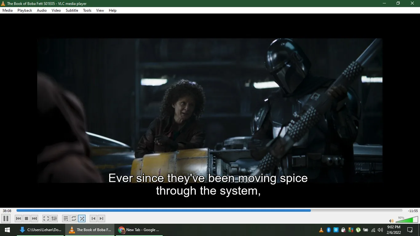 1) The screenshot captures a scene from the episode titled "The Book of Boba Fett S01E05," viewed using VLC media player. In an indoor setting, the image shows two characters engaged in conversation. On the left, a person with curly hair sits slightly forward, gesturing with their hands, suggesting engagement or explanation. On the right, a character in black Mandalorian armor holds a weapon. This armor is iconic within the Star Wars universe, reflecting the character's affiliation and role. The lighting is dim, creating a dramatic, sci-fi atmosphere typical of the series. The background reveals a workshop-like environment with machinery, reinforcing the setting's industrial feel. Subtitles at the bottom read, "Ever since they've been moving spice through the system," indicating dialogue related to storyline themes of trade or smuggling. The display features typical VLC interface elements, like the title at the top and playback controls at the bottom, confirming the media player being used.
2) On-screen text block:
- Title: "The Book of Boba Fett S01E05 - VLC media player"
- Captions / subtitles: "Ever since they've been moving spice through the system,"