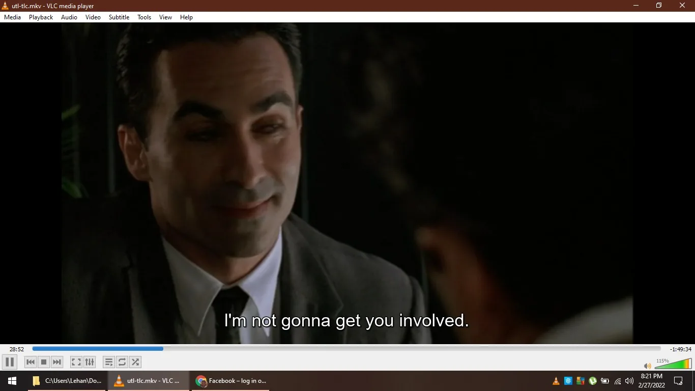 The image is a screenshot from a video being played on VLC media player, specifically a file named "utl-tlc.mkv". It shows a close-up of a man in a suit, engaging in a conversation with someone who is partially visible. The background is dark and the lighting is dim, suggesting an intimate or serious setting. The man's expression is subtle, possibly indicating a sense of reassurance or confidentiality as he says, "I'm not gonna get you involved," which is subtitled at the bottom of the screen. The interface of the VLC media player is visible, showing standard playback controls and the timestamp 28:52 of a total duration of 1:49:34. The taskbar at the bottom displays the date and time as 8:21 PM on 2/27/2022.