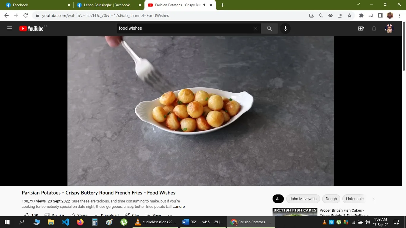 The image is a screenshot from a YouTube video titled "Parisian Potatoes - Crispy Buttery Round French Fries - Food Wishes." The channel name is "Food Wishes," and it is associated with John Mitzewich. The scene depicts a white dish filled with small, round, golden-brown potatoes, likely fried, garnished with chopped herbs. A hand is using a fork to pick one up, suggesting a casual and inviting presentation. The background is a smooth, gray countertop, adding to the kitchen setting. The lighting is soft, highlighting the dish's appealing texture and color. The video seems to focus on the preparation and cooking of these potato dishes, likely offering a recipe or cooking demonstration. The text below the video includes details about its views and publication date, indicating its popularity and relevance for those interested in cooking. The interface shows familiar YouTube elements like the play button, search bar, and recommendation tags.