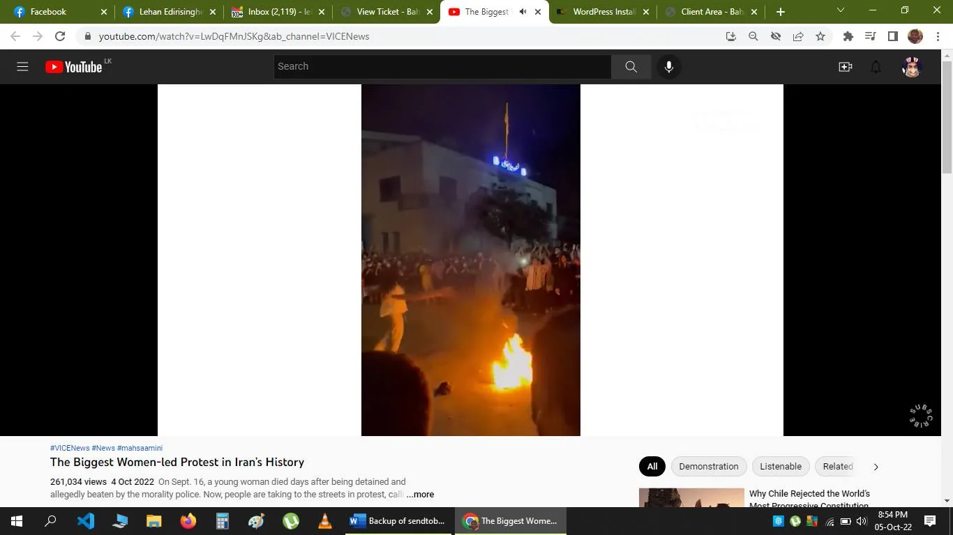 The screenshot captures a YouTube video page displaying a scene from a protest at night. Visible in the image is a crowd of people gathered around a fire. The crowd appears engaged, with some individuals standing close to the flames. The setting is outdoors, near a large building that is partially visible in the background. The fire illuminates the area, creating a dramatic contrast with the dark night sky.
The title of the video, "The Biggest Women-led Protest in Iran’s History," highlights the significance of the event being documented. The channel hosting the video, VICENews, is a well-known source for news content. The video's description mentions the context of the protest: following the death of a young woman named Mahsa Amini, people took to the streets in protest.
The interface shows several browser tabs open above the YouTube page, with ones labeled "Facebook," "Inbox," and "WordPress Install." The timestamp on the screenshot indicates it was taken on October 5, 2022, at 8:54 PM. The video has amassed a significant number of views, indicating widespread interest in the protest. The scene conveys a sense of urgency and solidarity among the demonstrators.