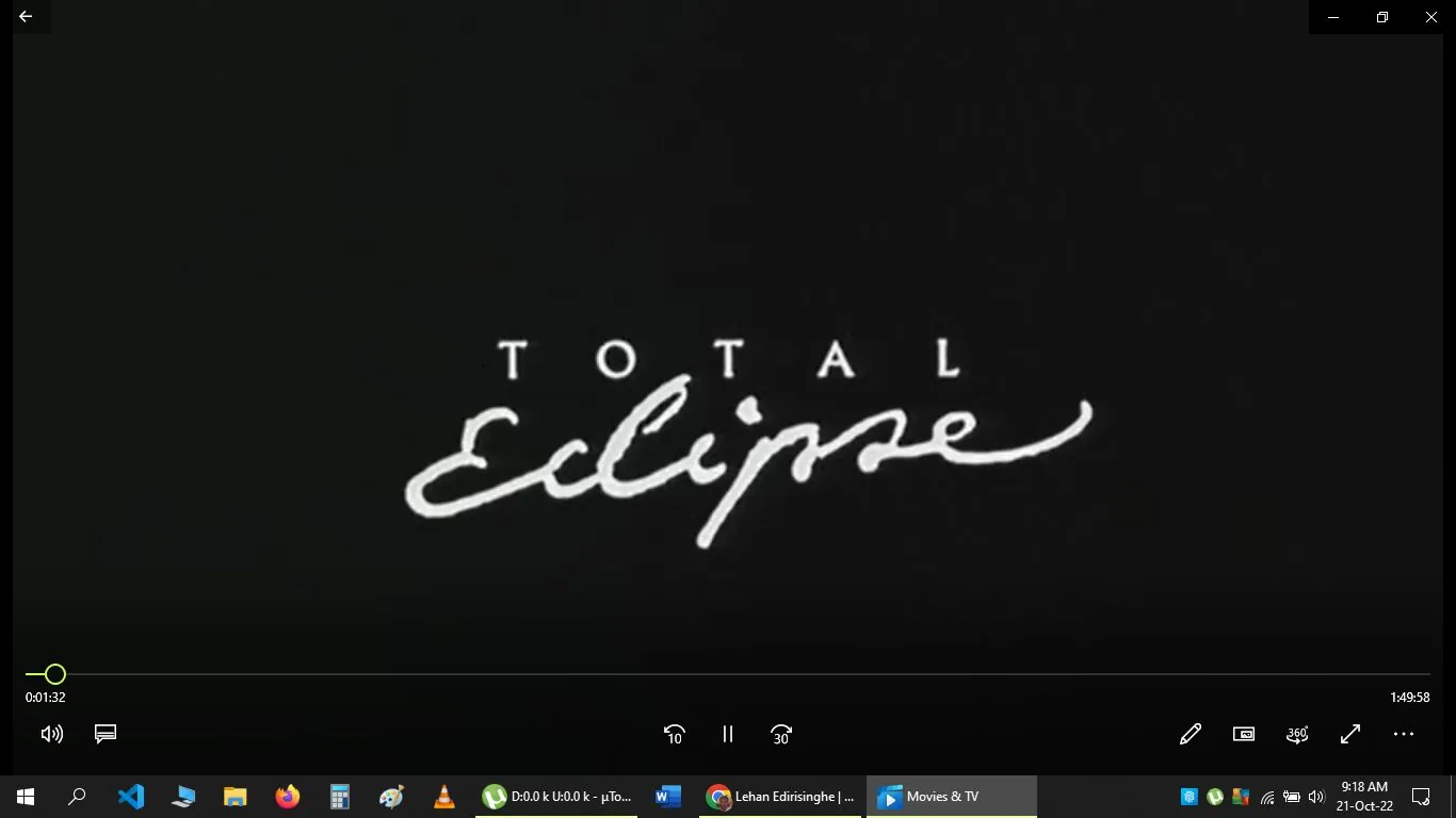 The image is a screenshot from a media player displaying the title screen of a film called "Total Eclipse." The text is written in a stylized white font against a black background, with "TOTAL" in uppercase block letters and "Eclipse" in a cursive script beneath it. The bottom of the screen shows typical media player controls and timeline, indicating a timestamp of 0:01:32 out of a total duration of 1:49:58. The "Movies & TV" app is being used, as indicated by the icon in the taskbar. The environment suggests a computer desktop with visible icons for applications like Microsoft Word, Firefox, and a media player. The overall mood is simple and formal, focusing on the film's title.