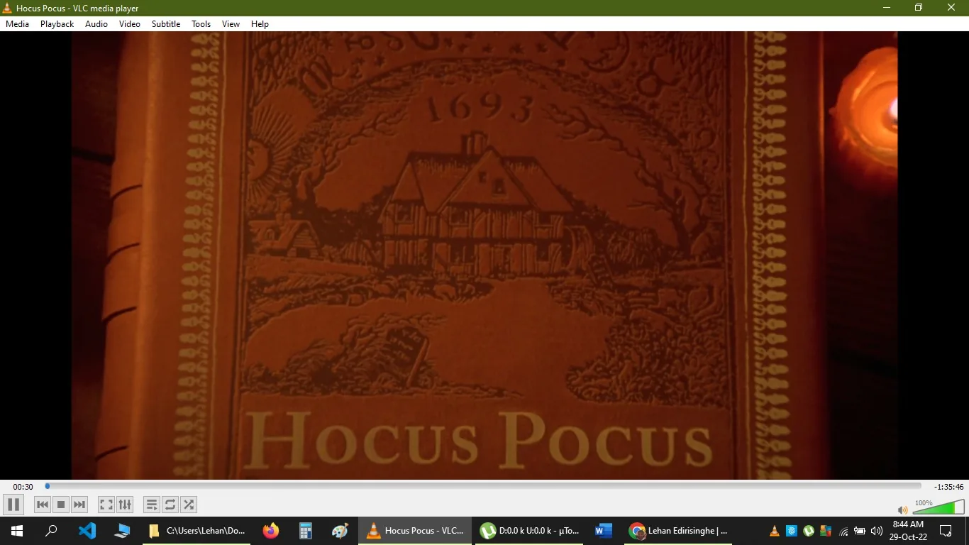 The image is a screenshot from the VLC media player, showing a scene from the movie "Hocus Pocus." The visual features an illustration of a house with the year "1693" prominently displayed above it. Below the illustration, the title "Hocus Pocus" is written in large, clear letters. The scene resembles an old book cover or a title screen with warm, earthy tones dominating the palette, giving it a vintage and mystical feel. The decorative border on the sides adds to the ancient, enchanted ambiance. This title screen sets the stage for the magical and historical elements of the film, hinting at its witchcraft theme. The scene is captured in a full-screen view, with VLC's media player controls visible at the bottom, indicating the user is 30 seconds into the film.