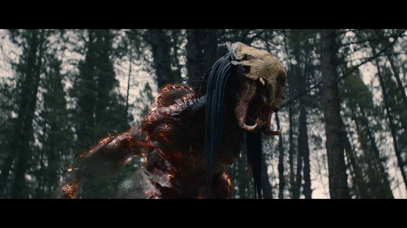 The image depicts a creature in a forest setting, likely from a science fiction or fantasy context. The creature has a menacing appearance, with a textured, glowing body that appears to be partially camouflaged or transitioning between visible states, suggesting advanced cloaking technology. Its head is adorned with a skull-like mask and long dreadlock-like appendages. The scene is set in a dense forest, with tall trees and diffused natural lighting creating an eerie atmosphere. The creature's posture is aggressive, indicative of an intense or confrontational moment. The lighting highlights the creature’s glowing, cracked skin, adding to the ominous mood. This visual seems to draw inspiration from familiar sci-fi themes involving invisibility and advanced technology, as referenced in the surrounding discussion about "Halo" and cloaking devices.