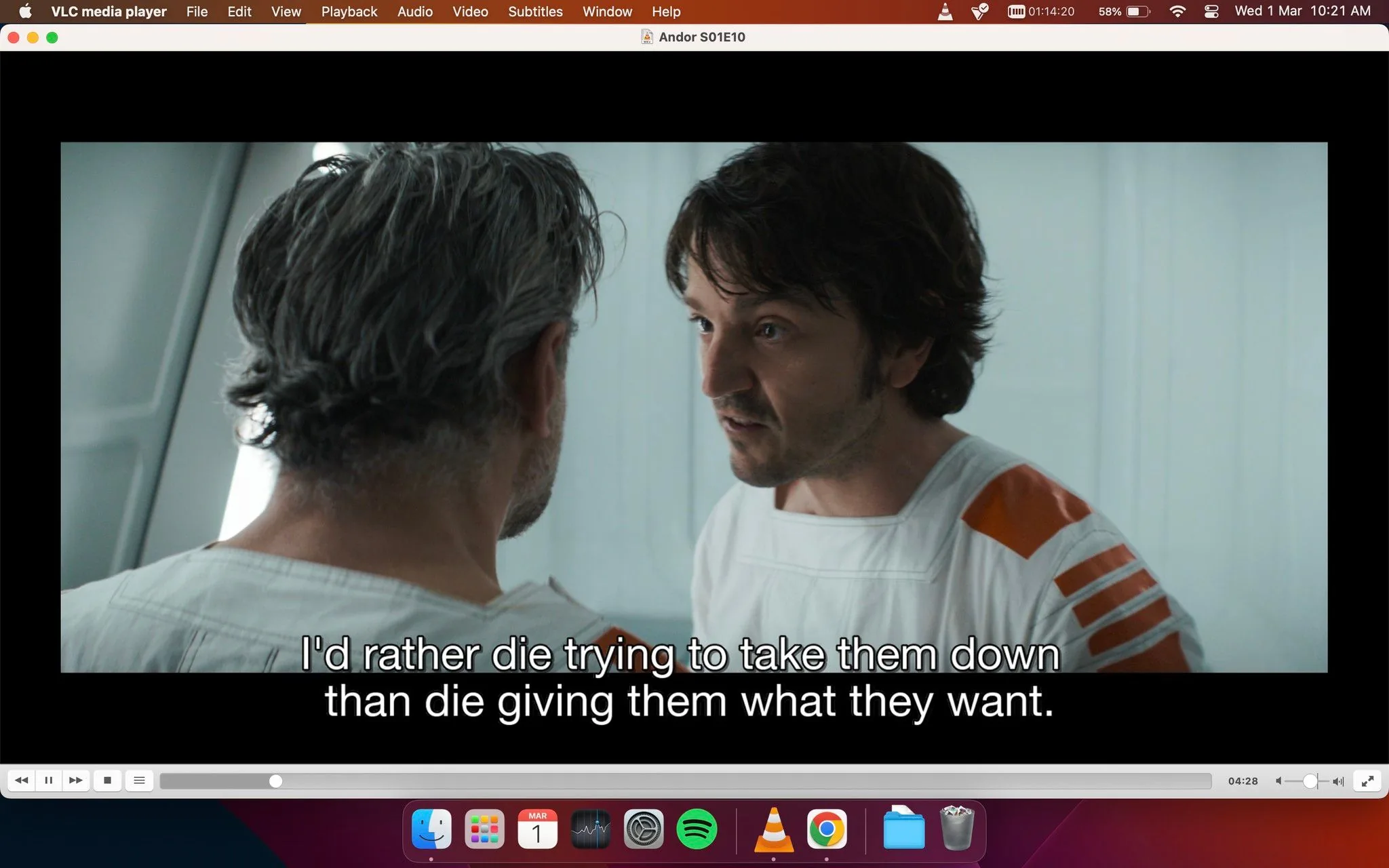 The screenshot depicts a scene from the series "Andor," specifically from Episode 10 of Season 1. It shows a tense conversation between two characters in a futuristic setting. The character on the right is speaking passionately, emphasizing his determination with the line, "I'd rather die trying to take them down than die giving them what they want." This dialogue suggests a theme of rebellion and resistance. The characters are dressed in white outfits with orange accents, typical of a sci-fi or prison environment. The lighting is bright and clinical, enhancing the serious and urgent atmosphere. The scene is being viewed on VLC media player, visible from the menu bar and controls at the top and bottom of the screen. The player shows a timestamp, indicating the viewer is 4 minutes and 28 seconds into the episode. The desktop background visible beneath the media player includes various app icons, including Finder, Mail, and Spotify.
