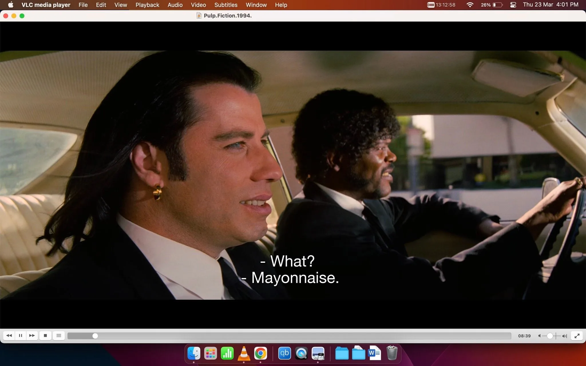 The image depicts a scene from the film "Pulp Fiction," showing characters Vincent Vega, played by John Travolta, and Jules Winnfield, played by Samuel Jackson, inside a car. The two are engaged in a conversation, as indicated by the subtitles "What?" and "Mayonnaise." Vincent, on the left, is wearing a suit with a white shirt, his long hair neatly slicked back, and an earring visible in his left ear. Jules, on the right, is also in a suit, with a tie, and has a distinctive curly hairstyle. The scene is shot in a car's interior during daytime, with light coming through the windows, illuminating the characters. The image is a frame from a video being played on VLC media player, as shown by the interface elements such as the play button, timeline, and file title at the top of the screen. The mood appears casual and conversational, typical of the film's iconic dialogues.