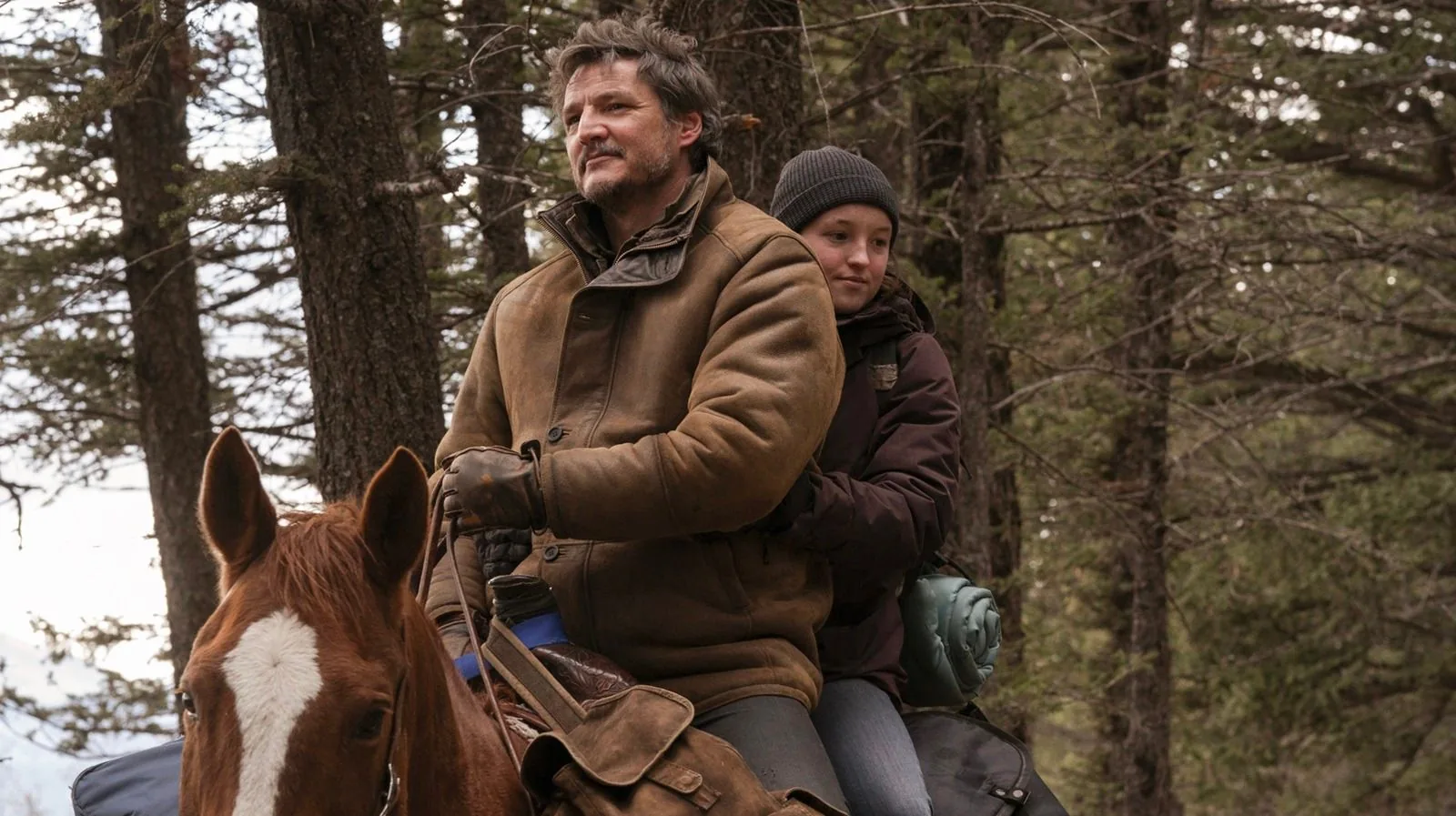 1) Rich description: This image features Pedro Pascal and Ellie from "The Last of Us" riding a horse through a forest. Pedro Pascal, in the foreground, is wearing a thick brown jacket, indicative of cold weather, and is seated at the front of the saddle. Ellie is seated behind him, wearing a dark jacket and a beanie, suggesting they are prepared for the elements. The pair is captured in a dense, wooded area with tall trees surrounding them, creating a natural, rugged backdrop. The horse they are riding is a chestnut color with a white marking on its face, adding a dynamic element to the scene. The expressions on their faces convey determination and focus, fitting the adventurous and dramatic tone of the series. The lighting is natural, with the trees casting shadows and the sunlight filtering through the branches. The scene captures a moment of travel and companionship, central themes in the series.
2) On-screen text block:
- Title: "The Last of Us"
